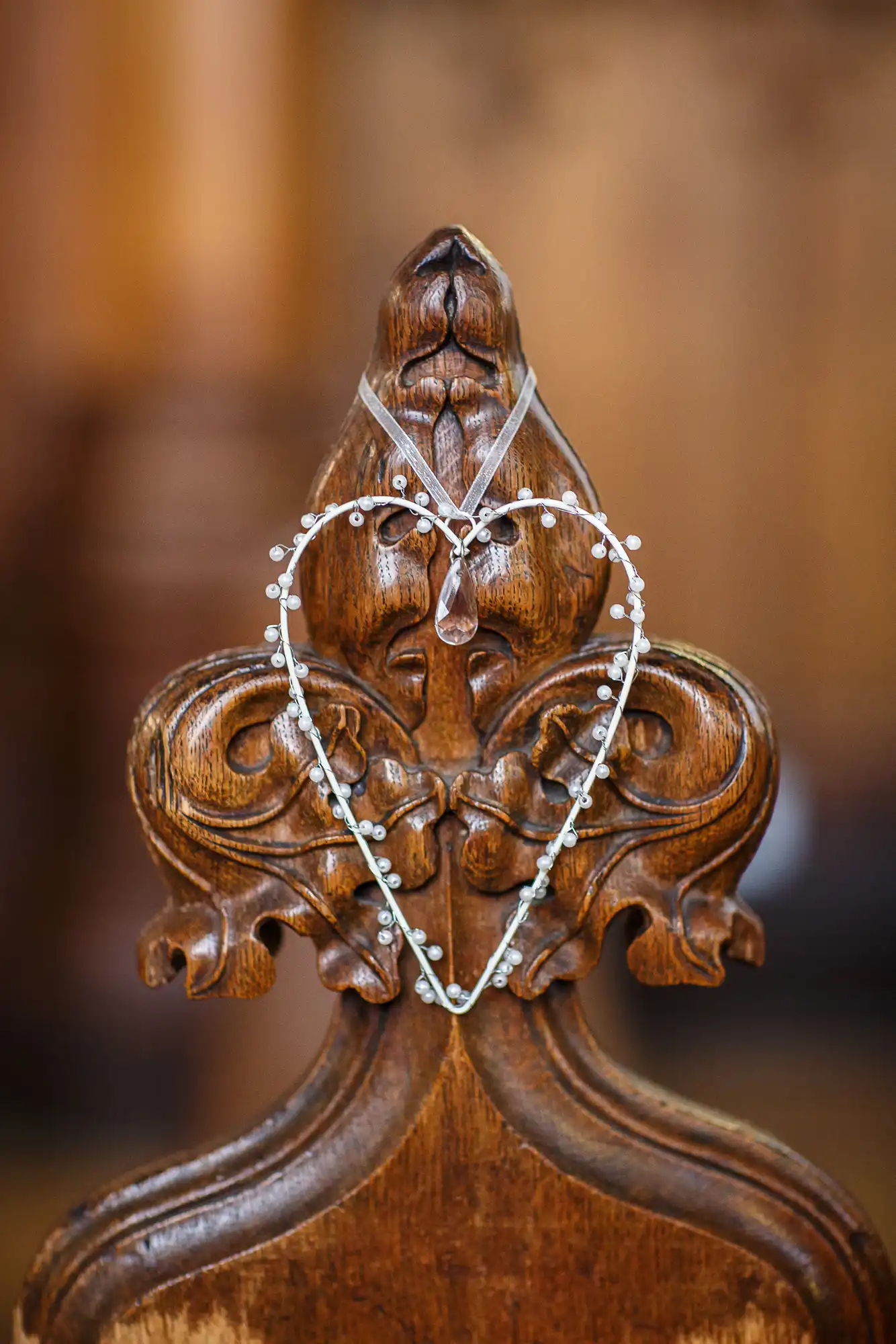 A delicate tiara rests on a carved wooden chair with an ornate backrest, set against a softly blurred background.