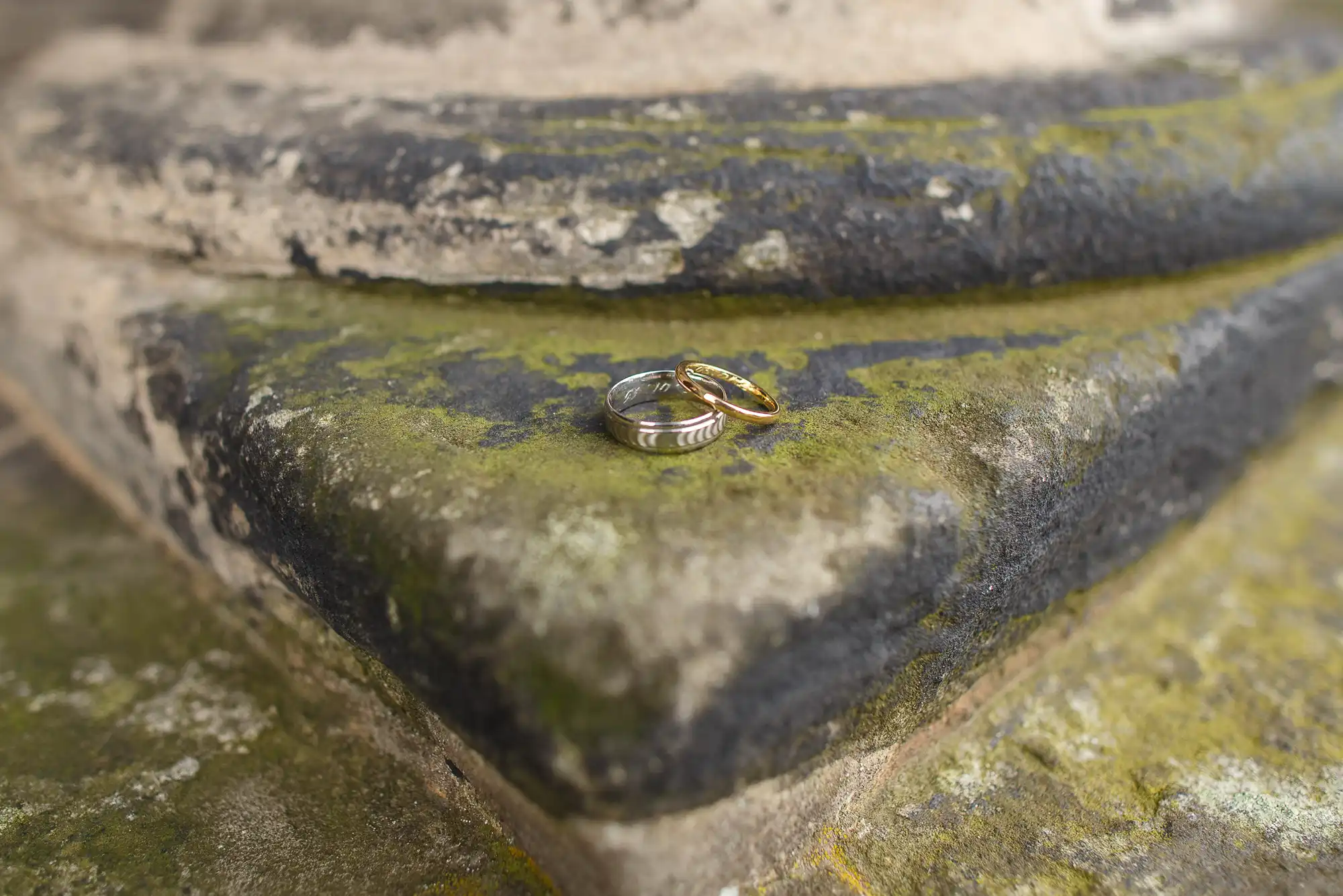 Two wedding rings resting on a moss-covered stone step with a focus on the texture of the moss and stone.