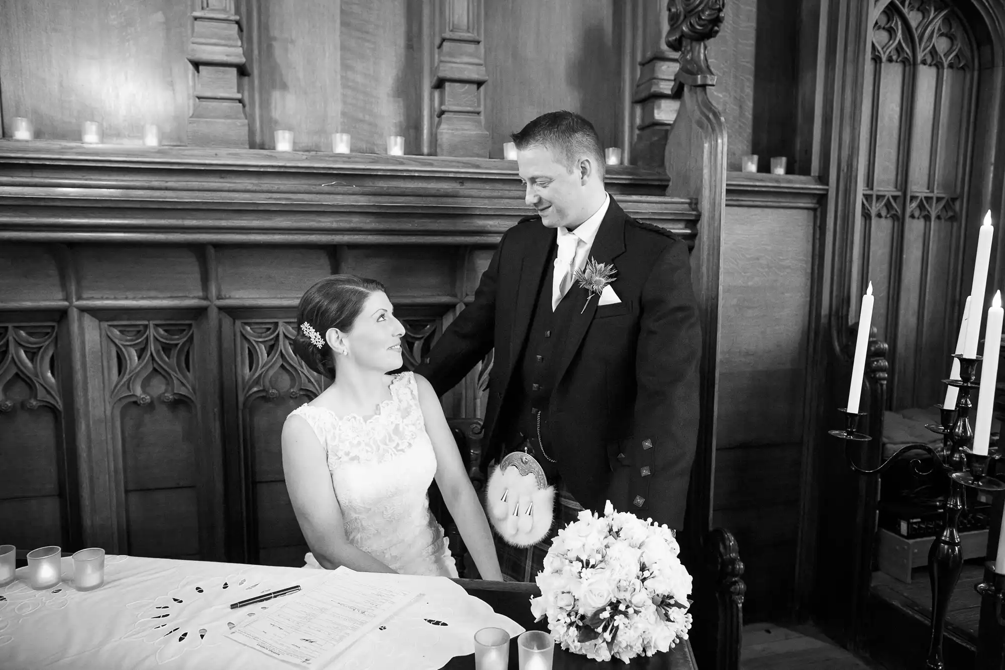 A bride and groom smiling at each other at the signing table inside a church, black and white photo.