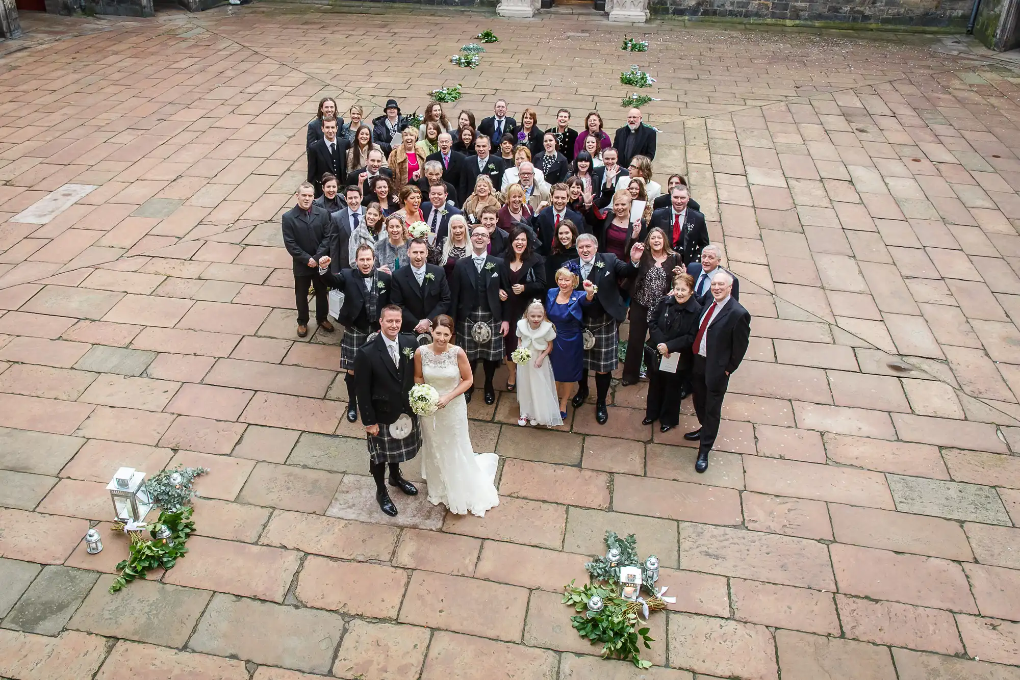 Aerial view of a large wedding group posing in a courtyard, with the bride and groom at the front center.