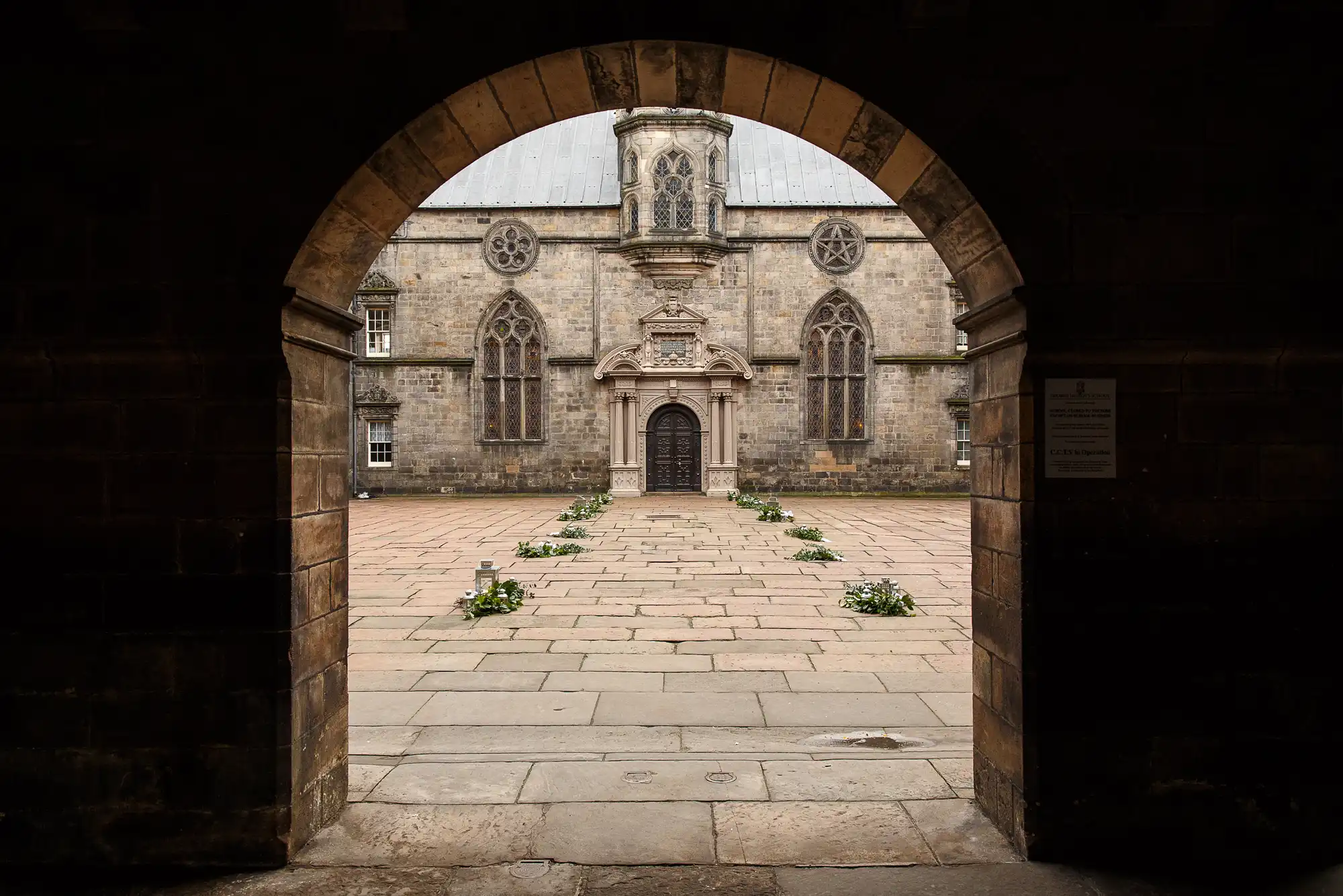 View of an historic stone building with a central arched entrance, seen through a large stone archway.