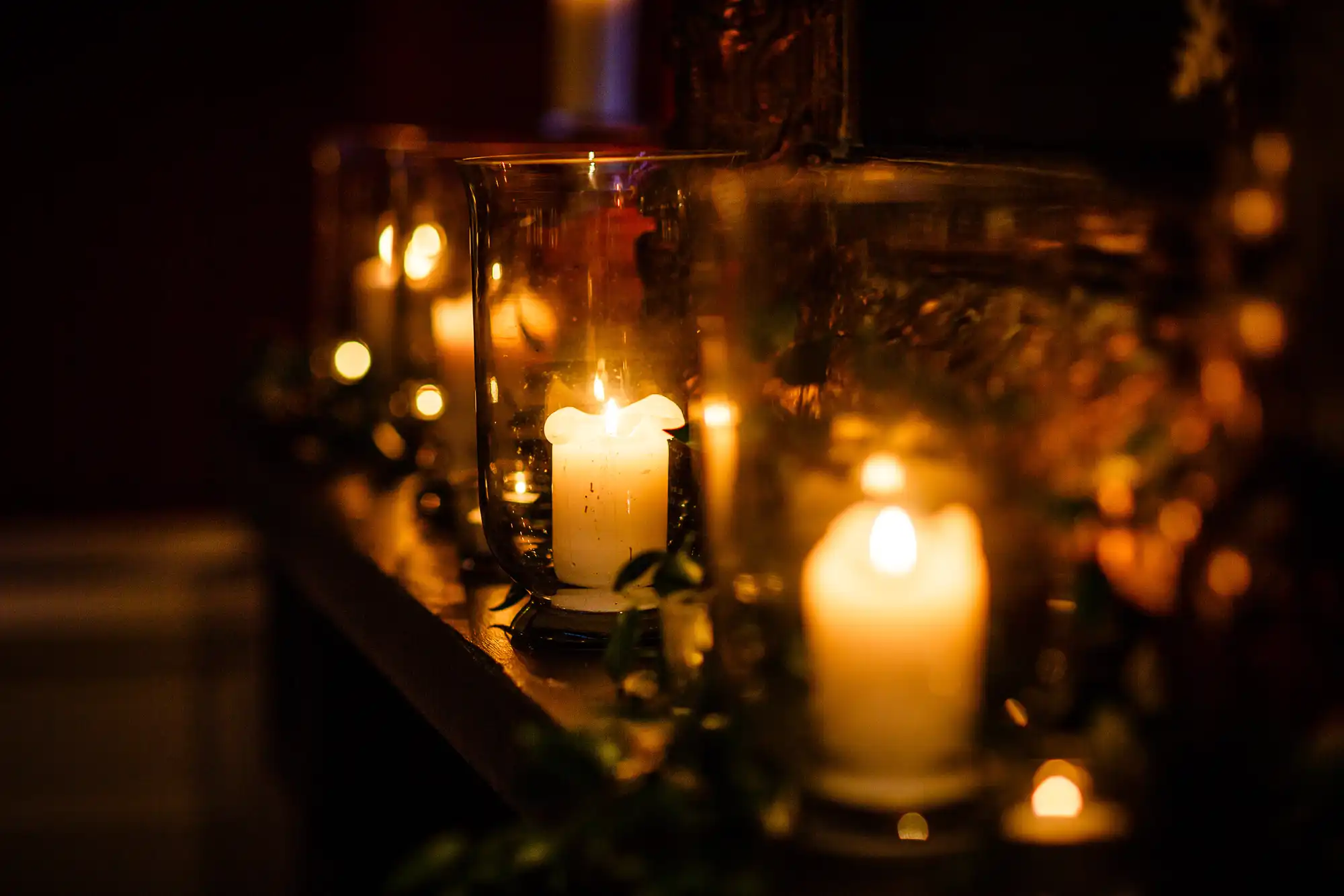 Candles glowing warmly inside glass holders, adorned with festive decorations on a shelf.