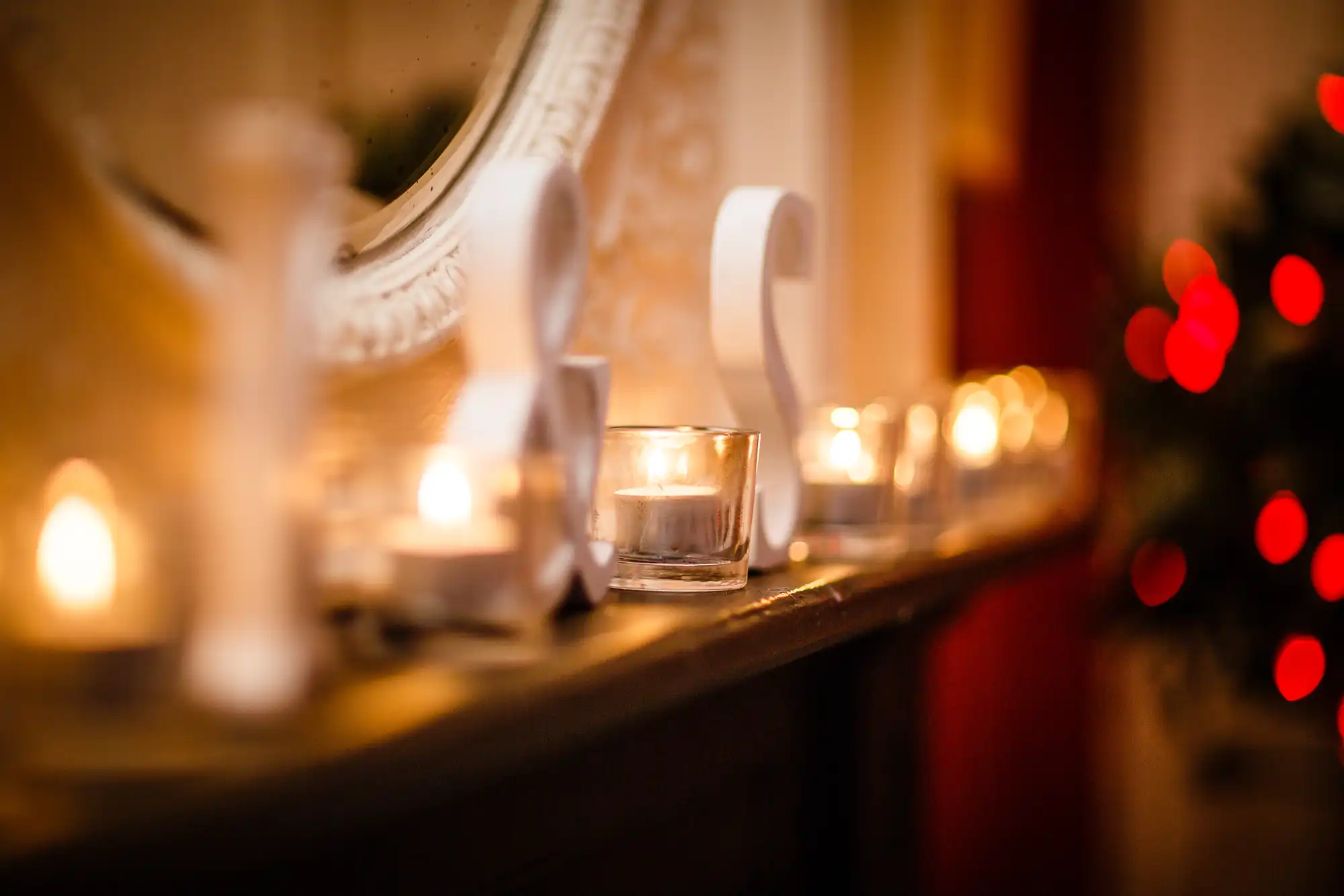 Lit candles in small glass holders on a mantel, with a mirror and soft glow, creating a warm, festive atmosphere.