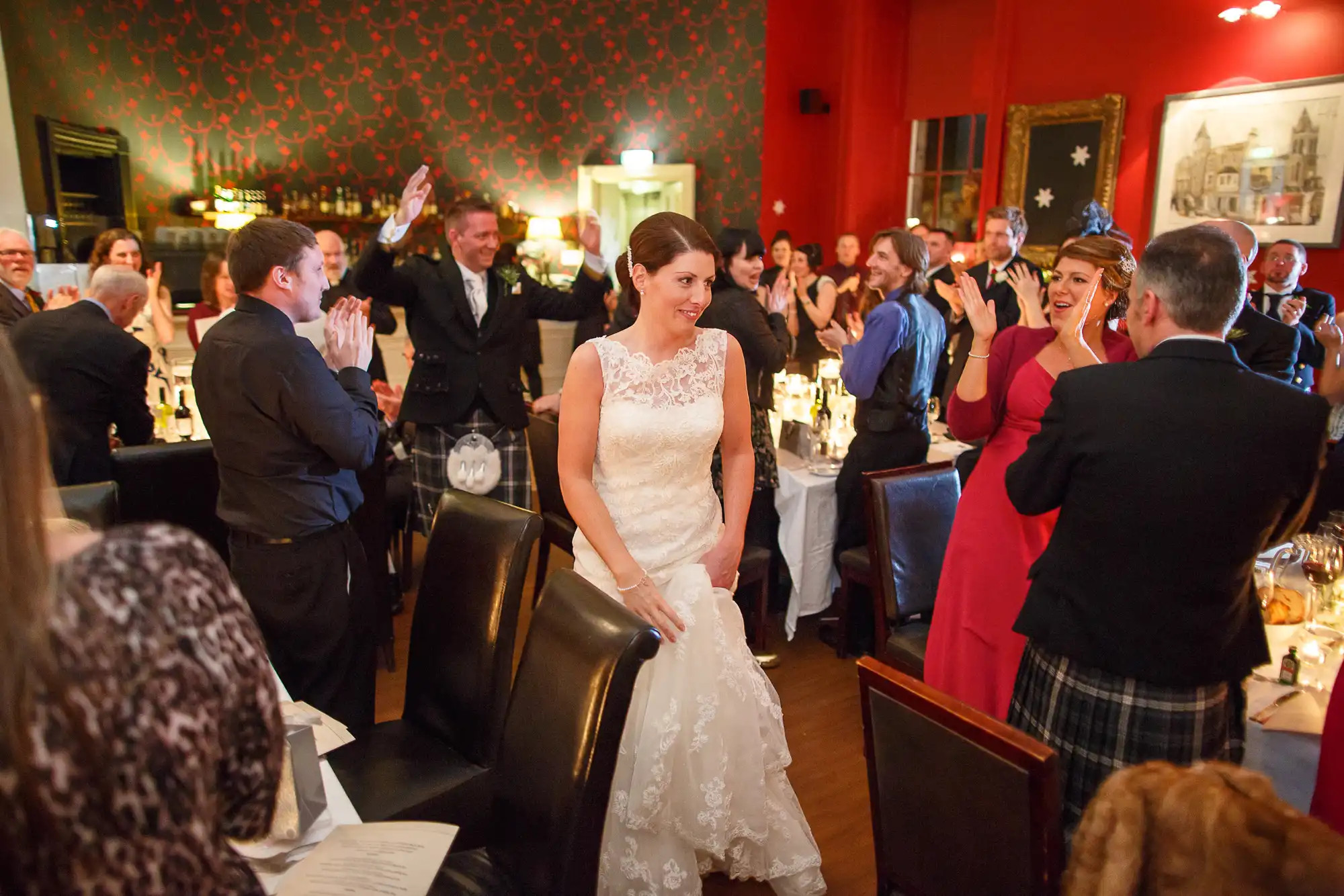 A bride walking through a restaurant during her wedding reception, being applauded by guests.