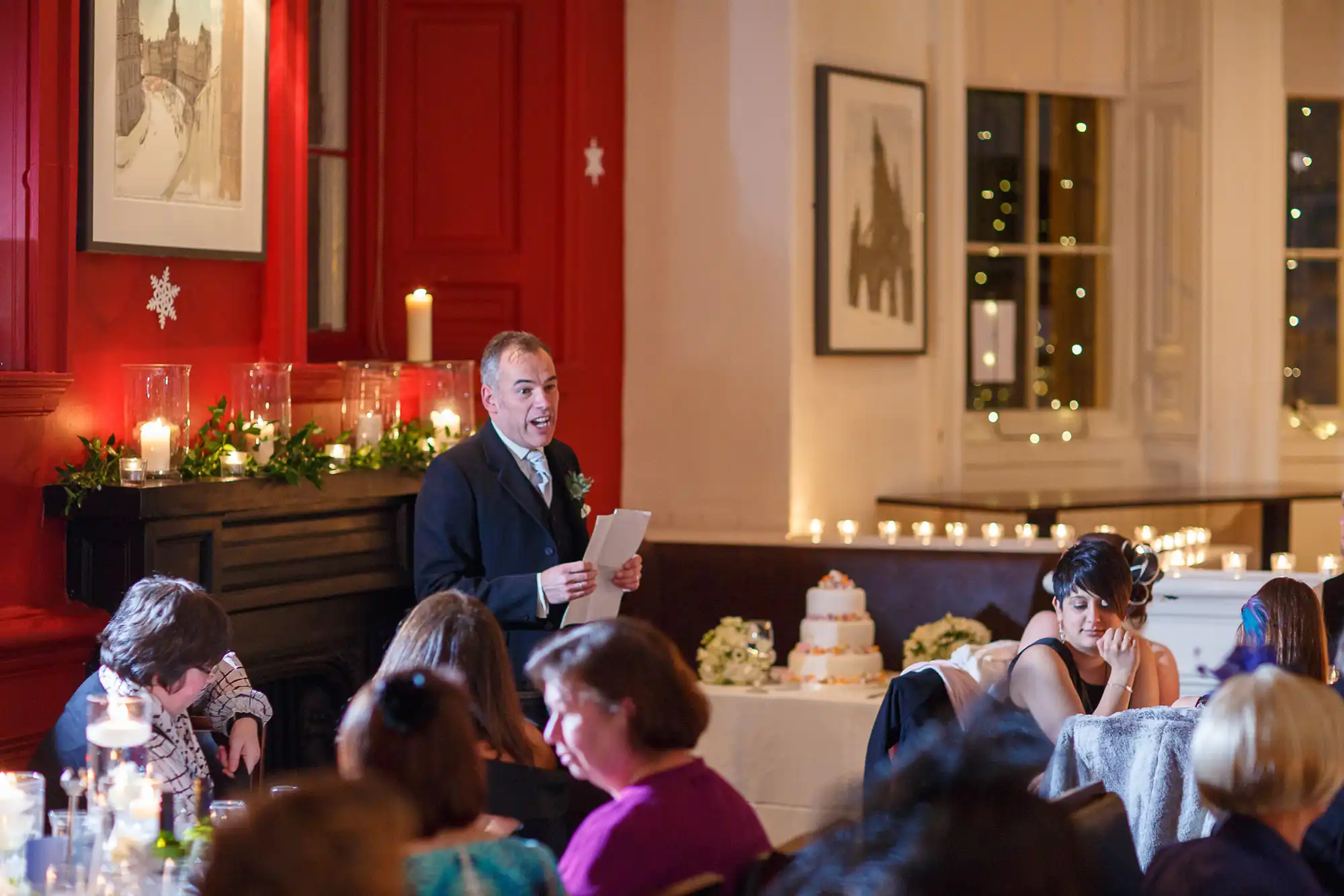 Man giving a speech at a wedding reception, with guests seated around tables and a bride listening intently. the room features festive decorations and ambient lighting.