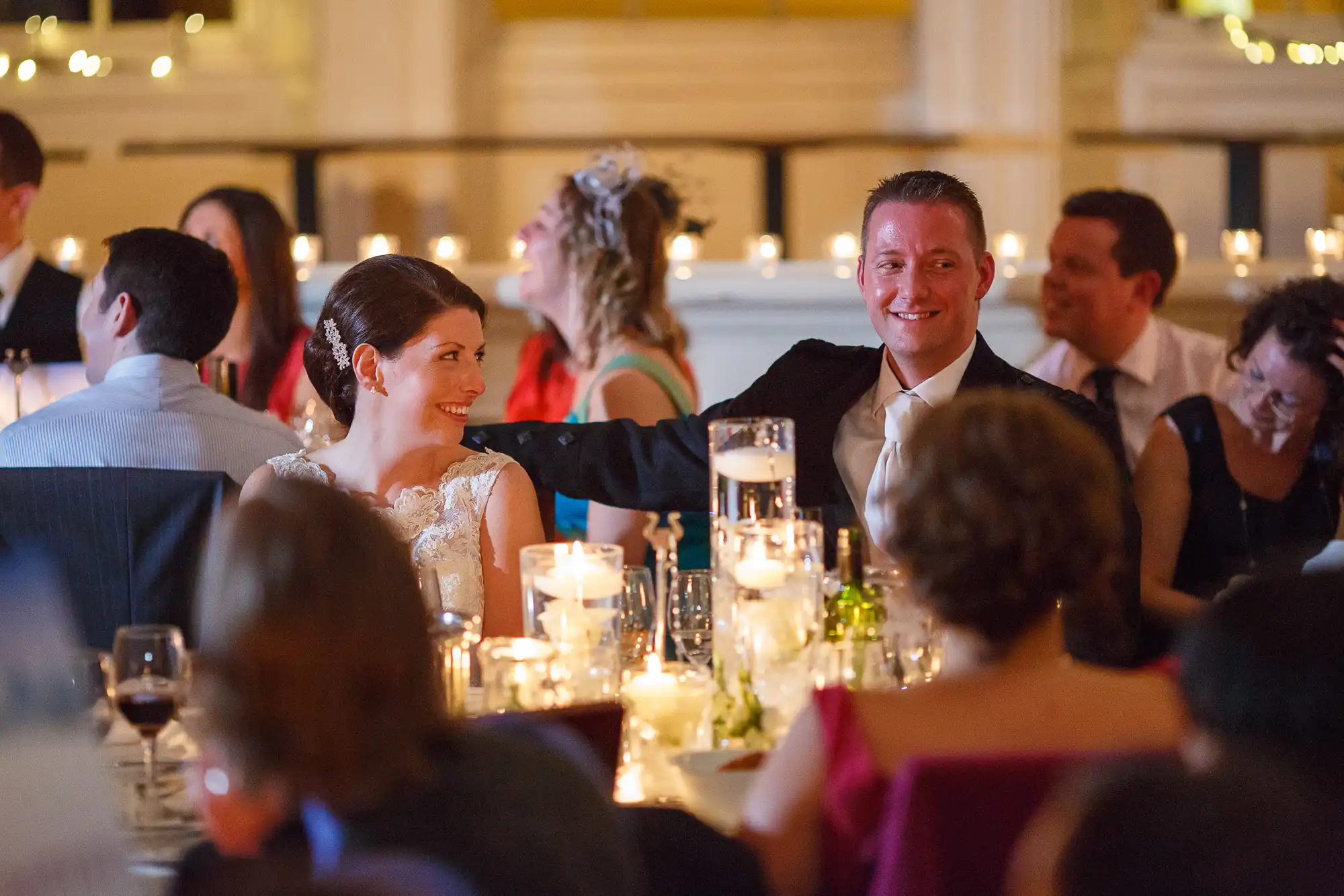 A bride and groom smiling and interacting with guests at a wedding reception dinner.