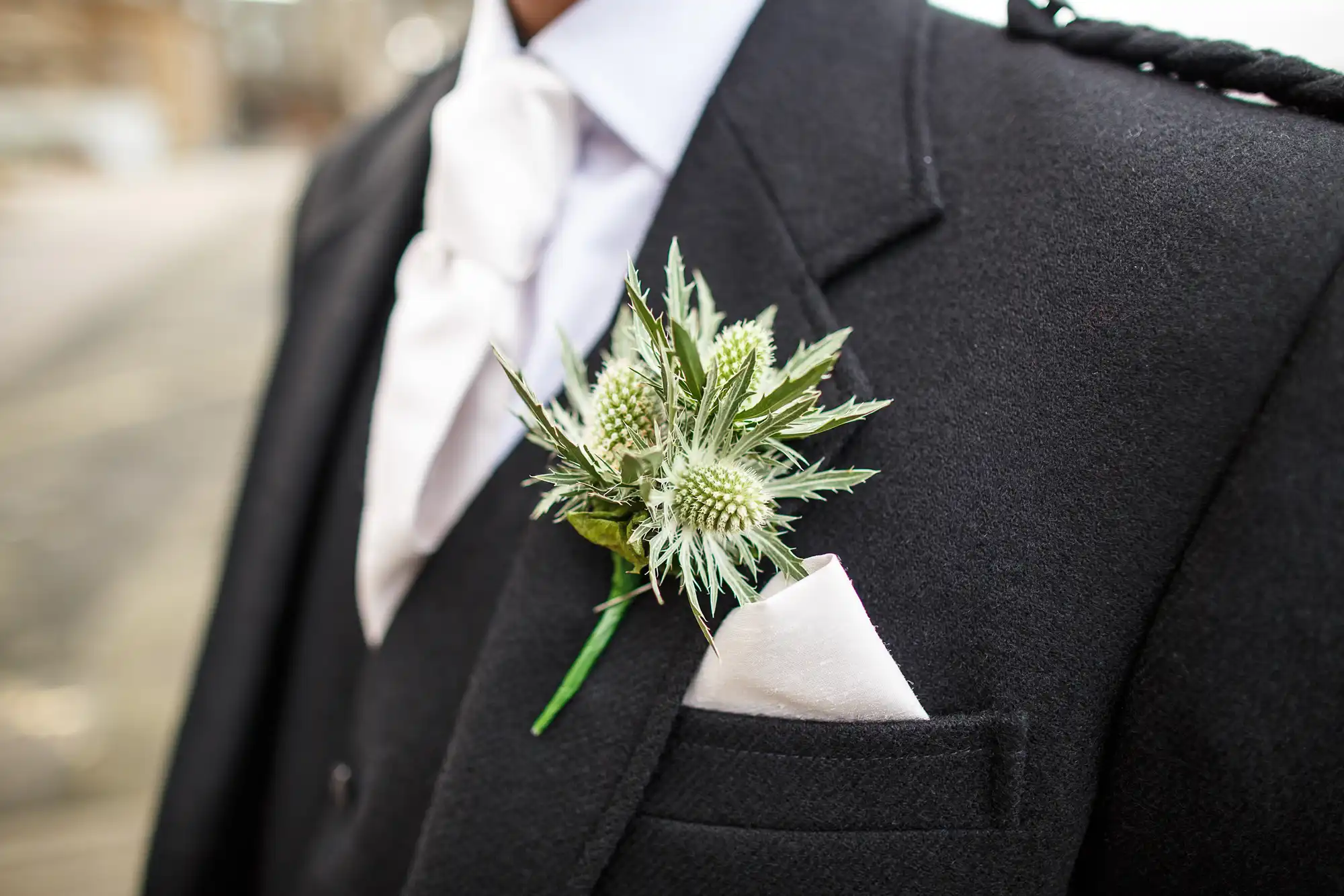 Close-up of a man in a black suit with a white shirt and pocket square, adorned with an unusual spiky green boutonnière.
