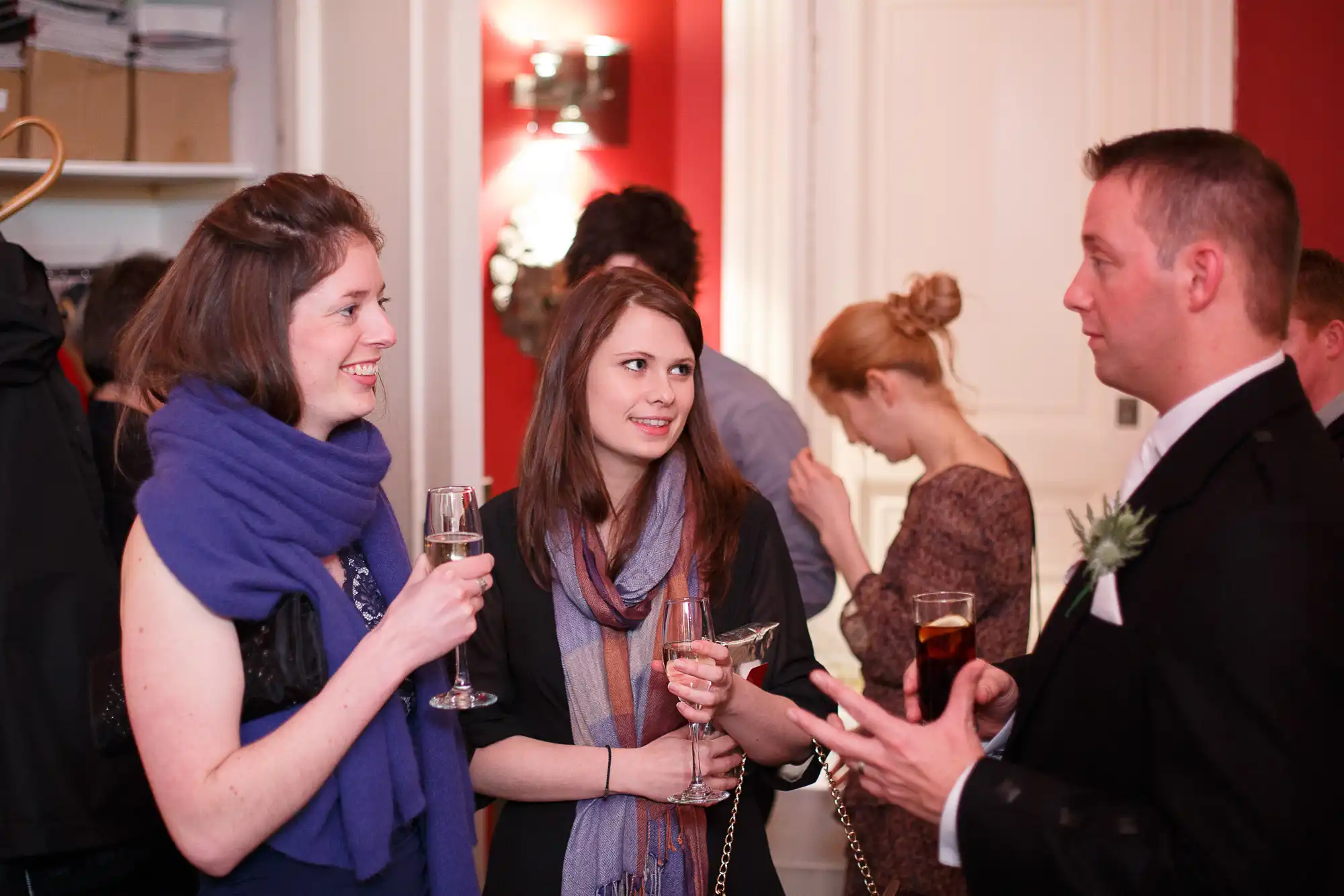 Three people engaging in a conversation at a social event, two women and a man, holding glasses of champagne.