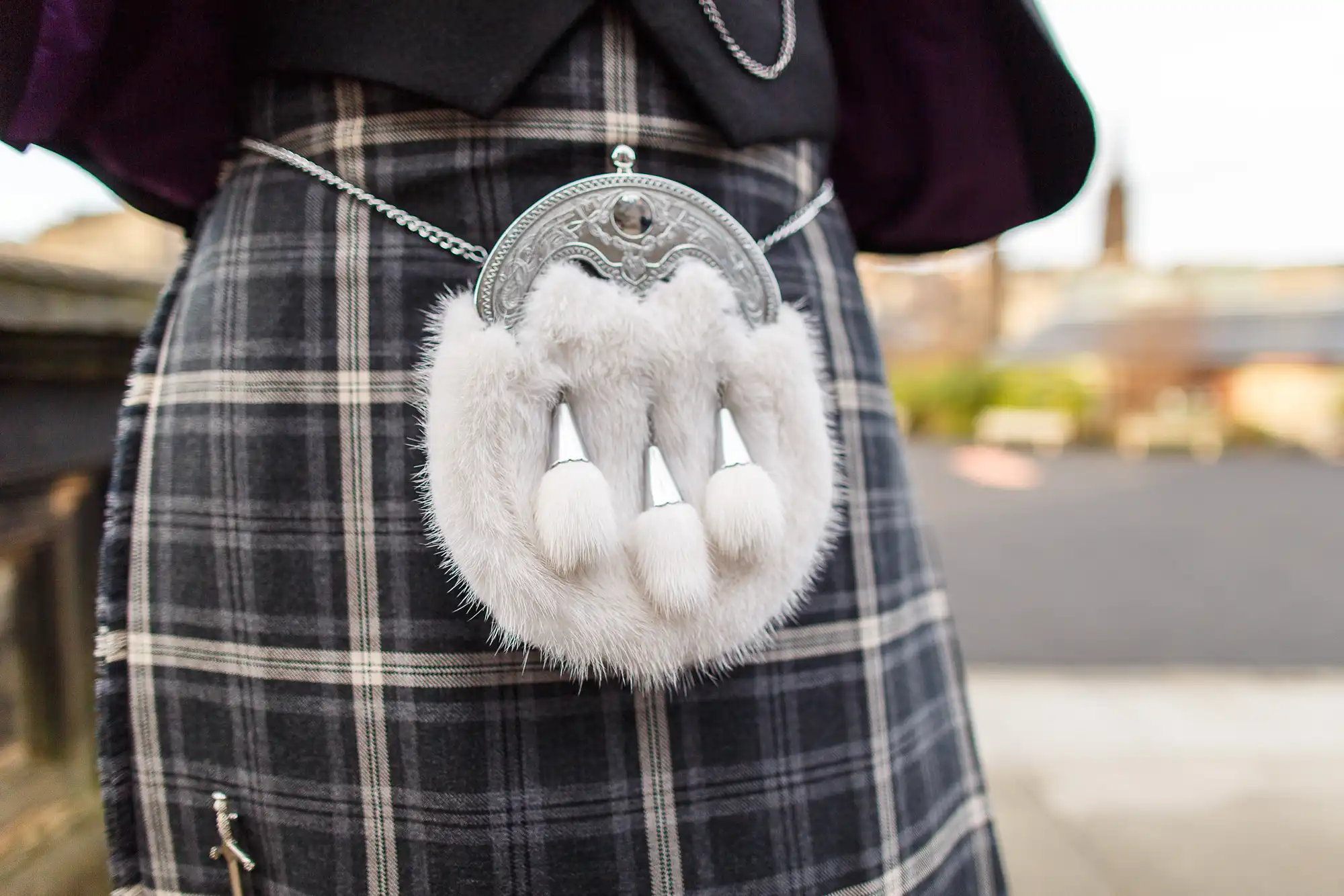 Close-up of a traditional scottish sporran made of white fur and metal, attached to a tartan kilt.