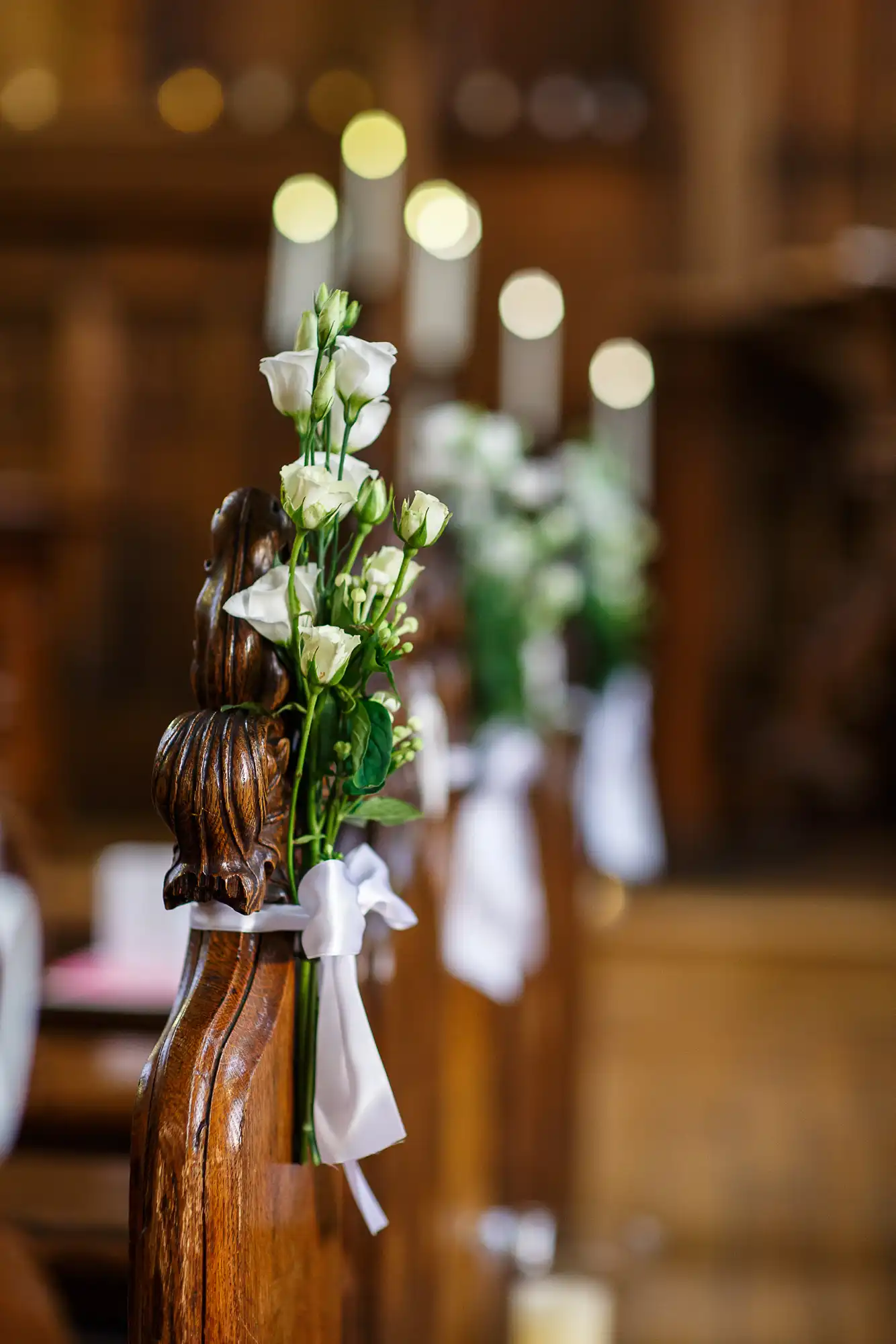 White flowers and ribbons decorate wooden pews in a church, with blurred background highlighting the interior architecture.