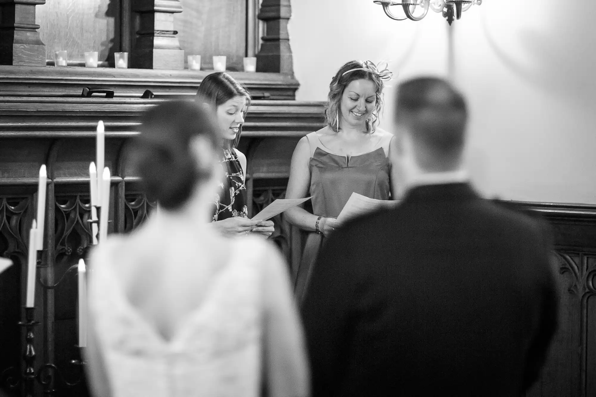 A bride and groom listen to a woman officiating their wedding in a church, captured in black and white.