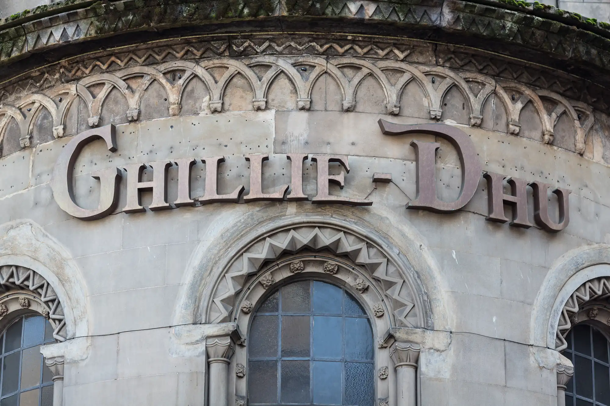 Close-up of a building's ornate facade featuring the words "chilli life dao" in a cursive, metallic script, with arches and detailed stone carvings.