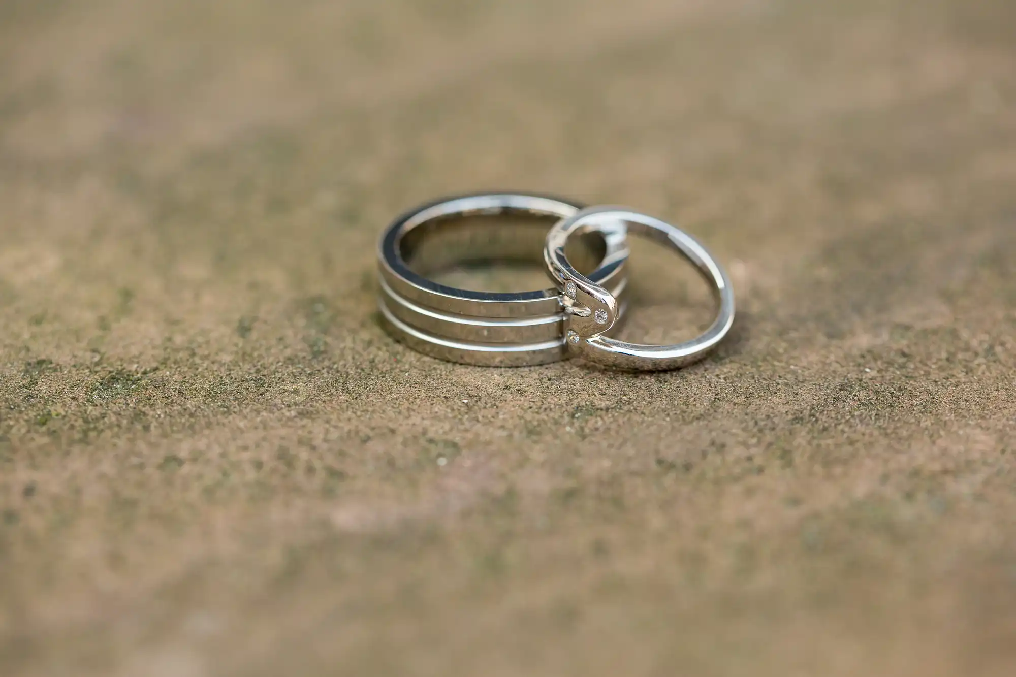 Two intertwined silver wedding rings placed on a textured surface, one ring featuring a small diamond.