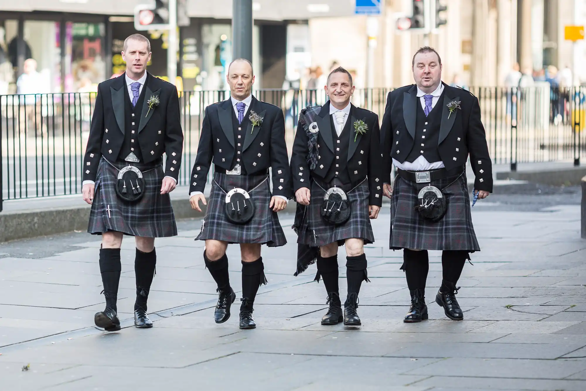 Four men dressed in traditional scottish kilts with sporran, walking down a city street, likely headed to a formal event.