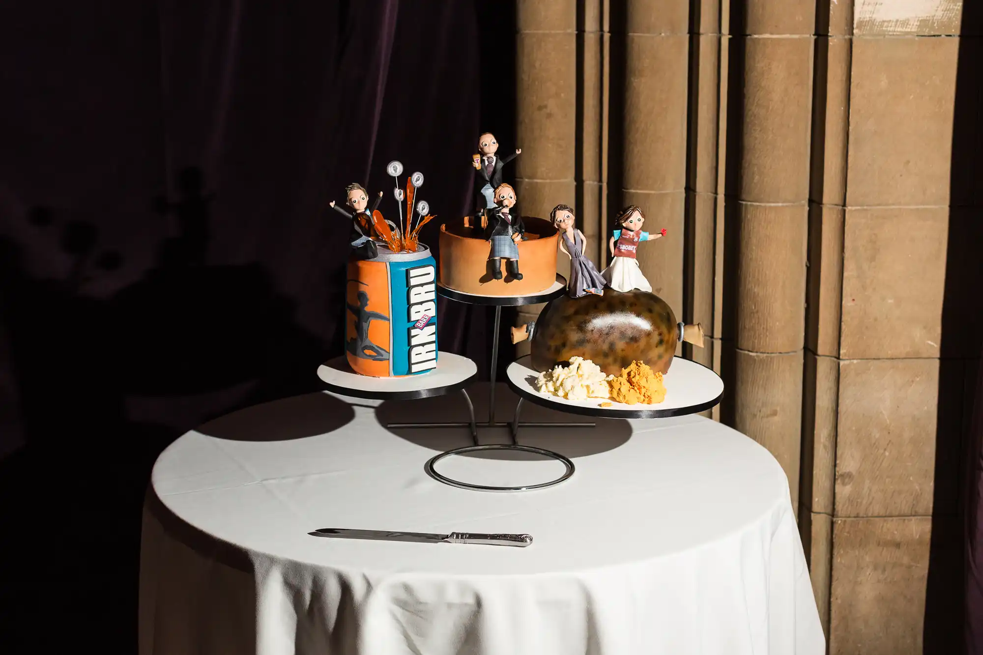 A unique wedding cake display featuring three tiers with customized figurine toppers representing different personal interests, illuminated by spotlight.