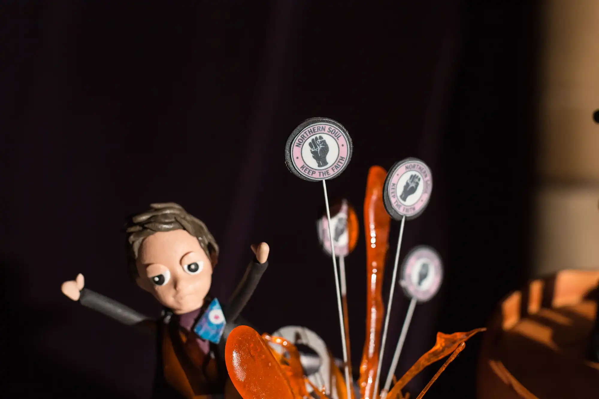 A model of a character resembling a pilot beside pinwheel-like structures with airplane cockpit instrument designs, against a blurred dark background.