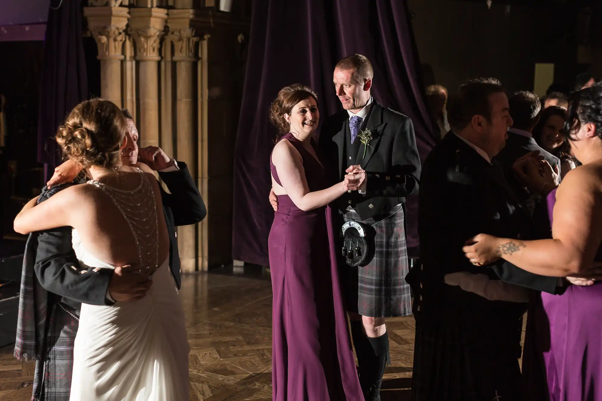 Couples dancing at a formal event, with one man in a kilt and women in elegant dresses.