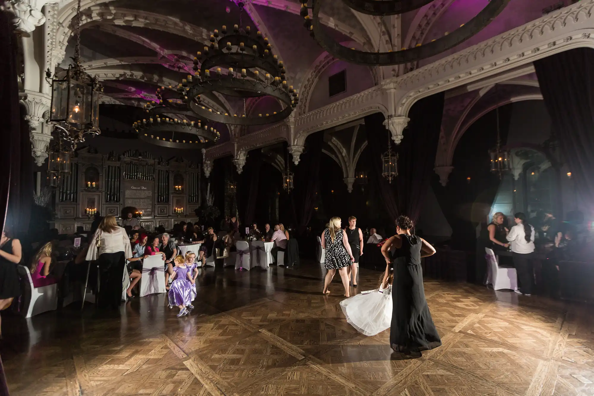 Elegant ballroom with guests dancing under dim, warm lighting and a classic architectural backdrop with arched ceilings and intricate details.