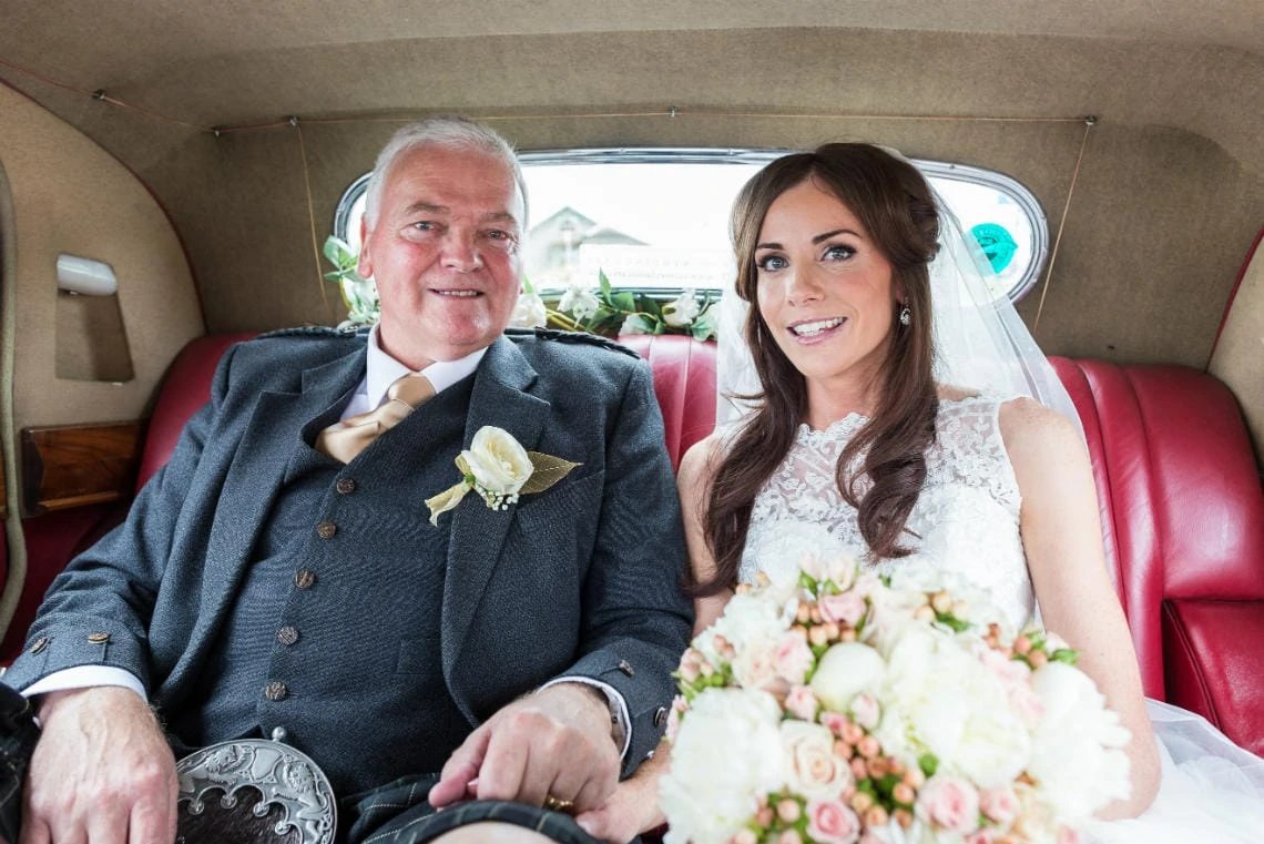 bride and her father sitting in the back of a classic wedding car