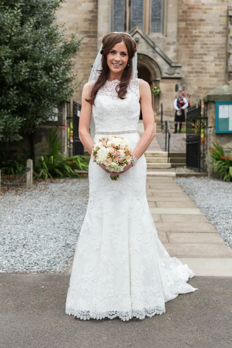 bride holding her bouquet outside the church in East Lothian with piper playing in the background
