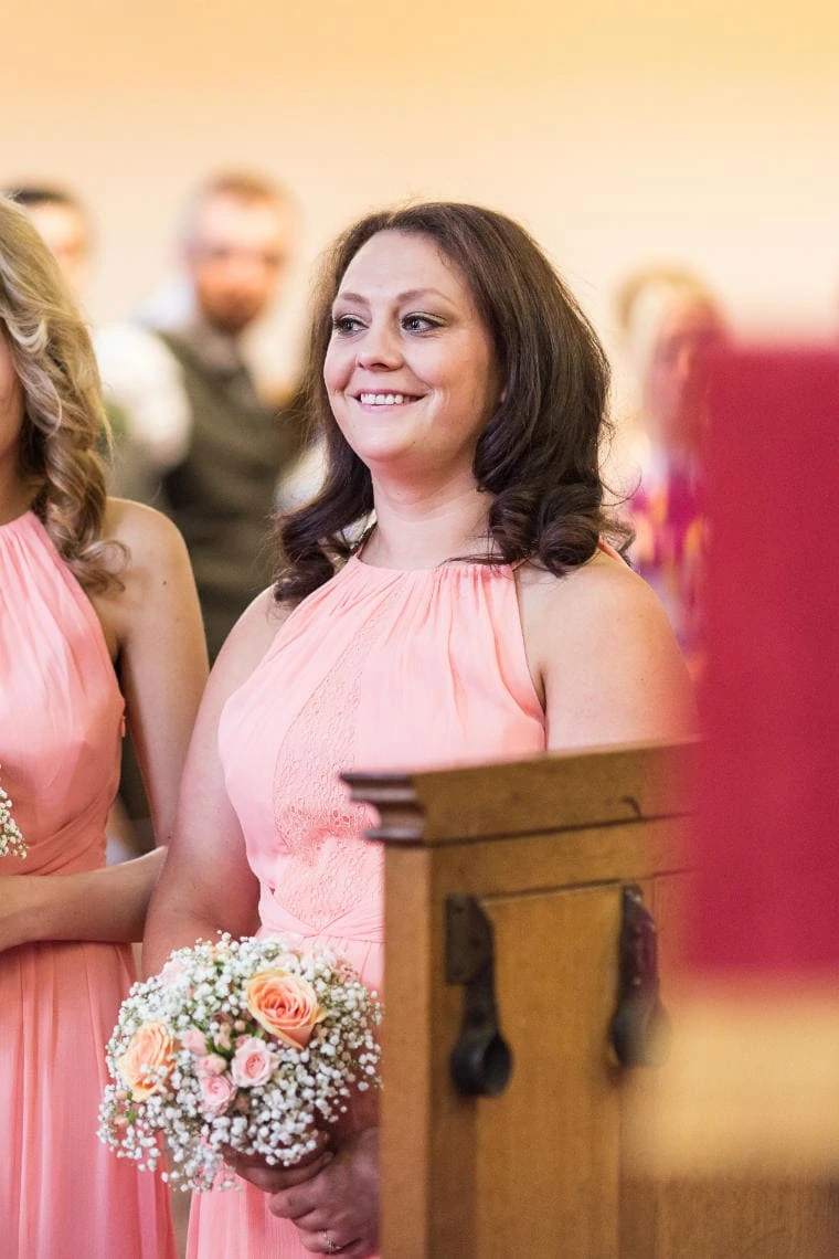 bridesmaid smiling as bride and groom exchange vows and rings at the church in East Lothian