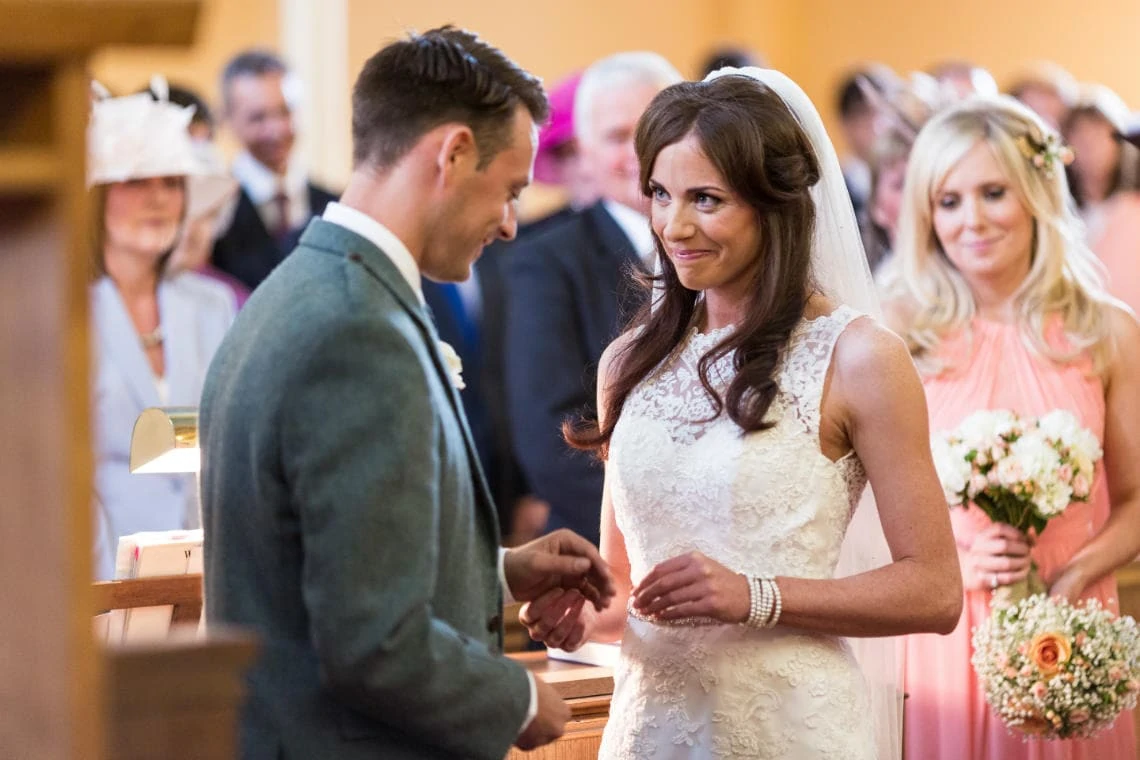 bride smiles at groom during the exchange of rings in the church in East Lothian