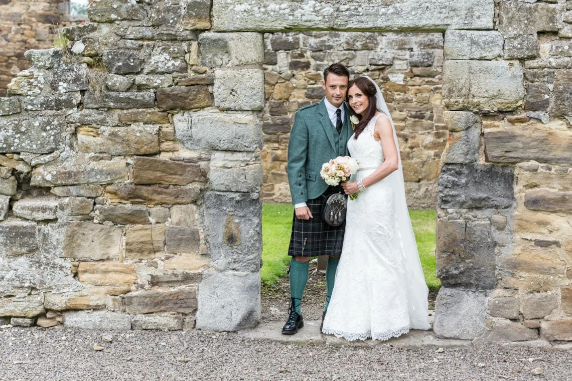 newlyweds standing beneath a stone doorway at the rear of at the church in East Lothian