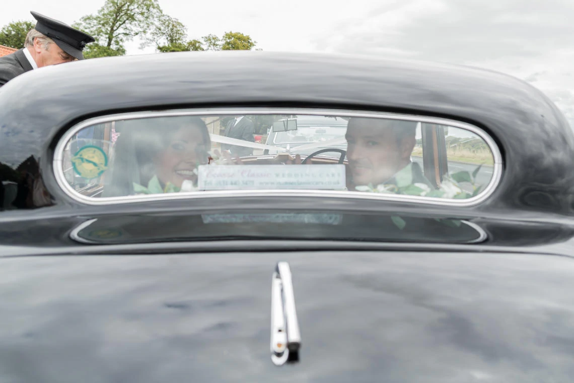 newlyweds smiling as they look out the rear window of a classic wedding car
