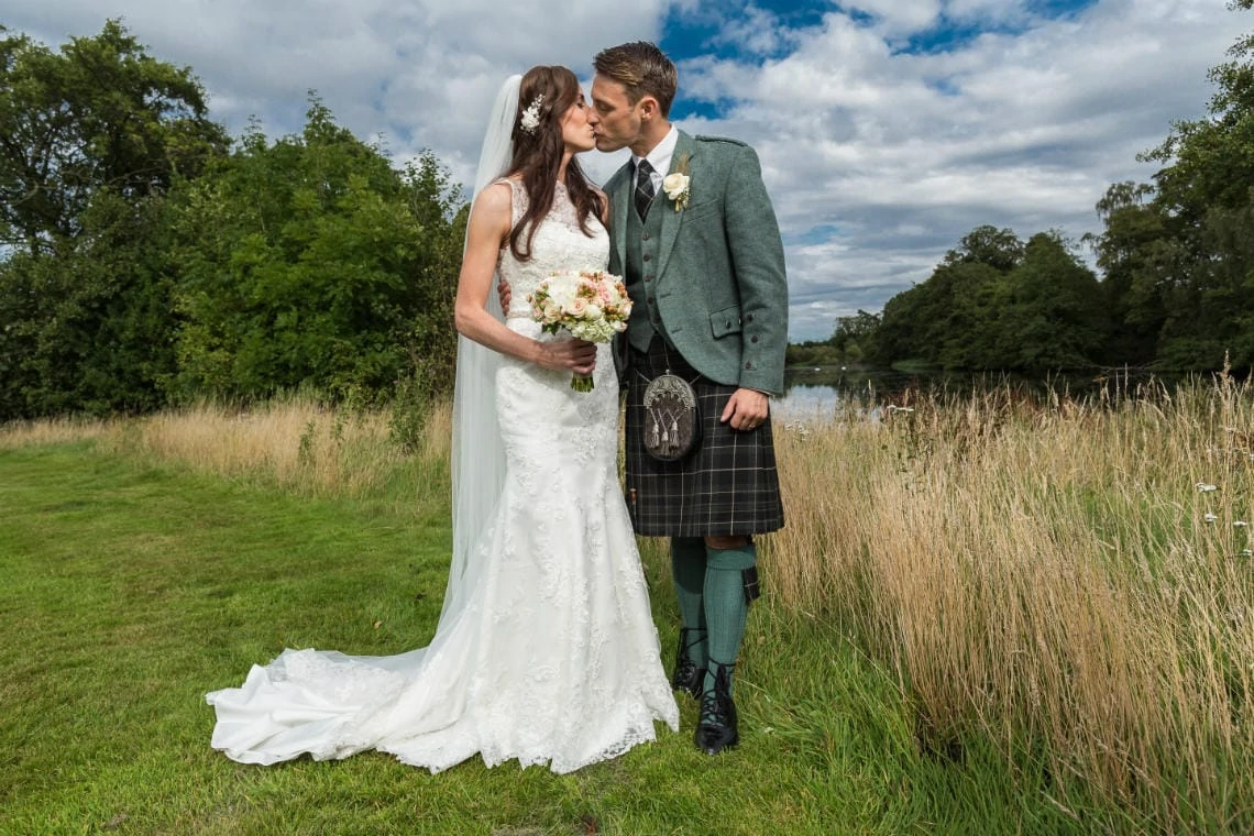 newlyweds kiss with the pond in the background on the golf course of the Dalmahoy Hotel