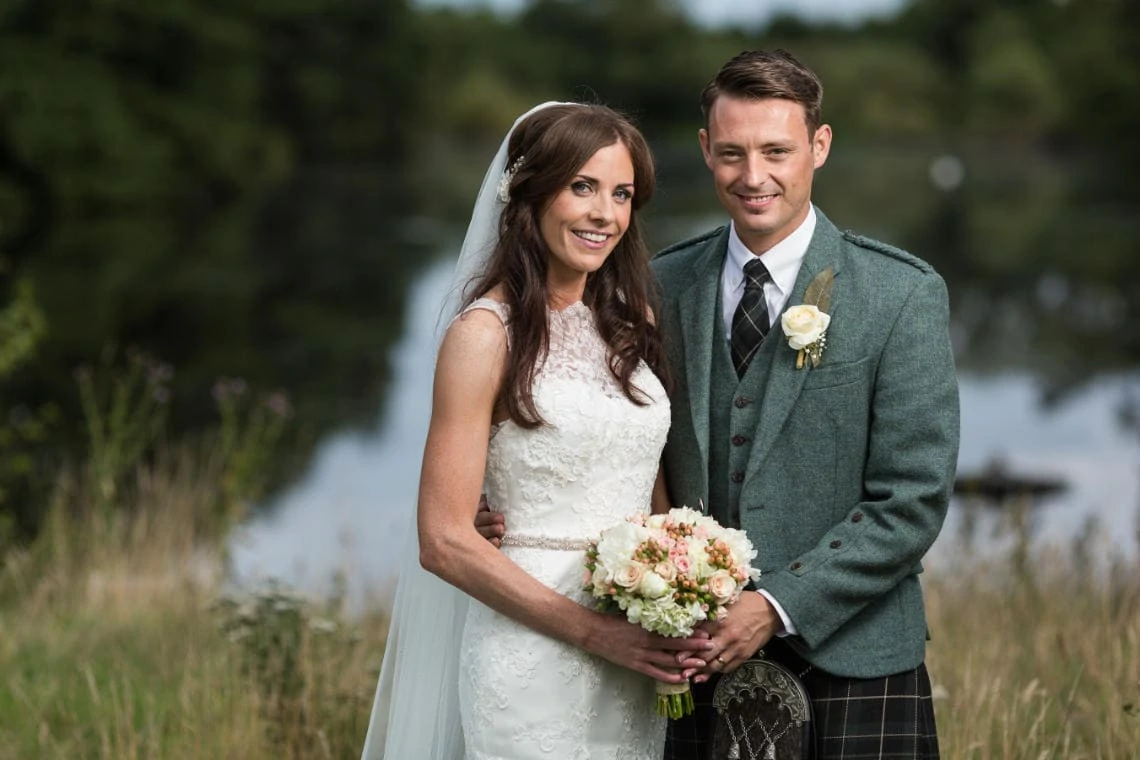 newlyweds embrace with the pond in the background on the golf course of the Dalmahoy Hotel