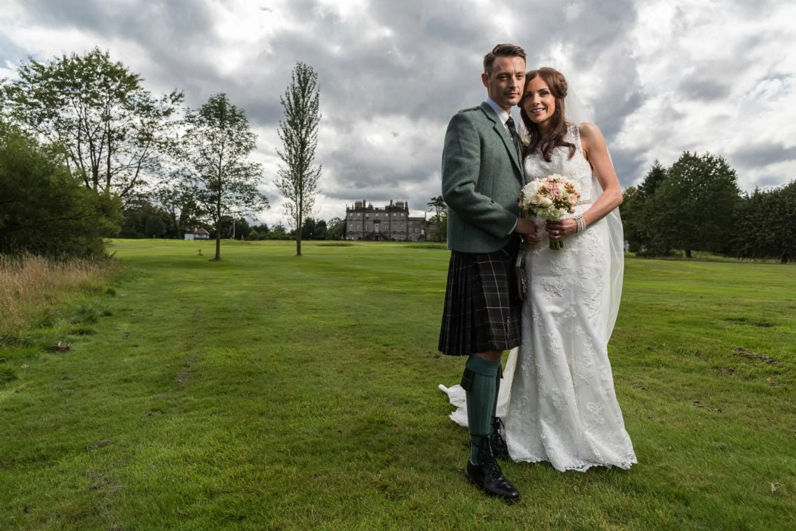 newlyweds on the golf course with the Dalmahoy Hotel in the background