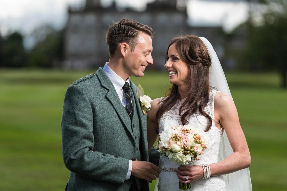 newlyweds laughing on the golf course with the Dalmahoy Hotel in the background