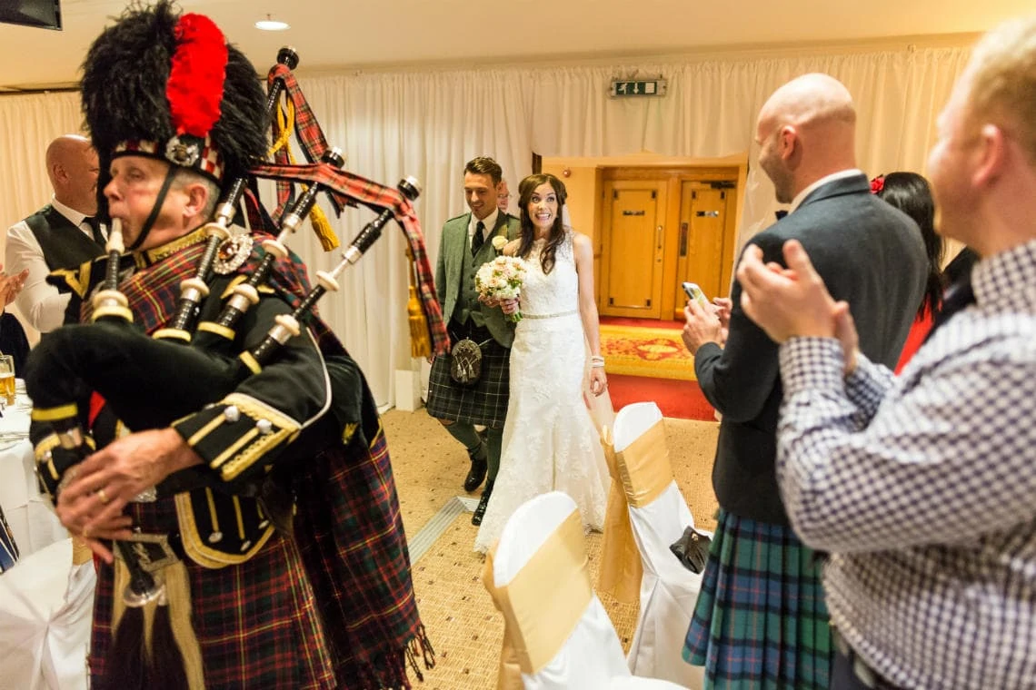 newlyweds are led by the piper to the top table in the Dalmahoy Suite