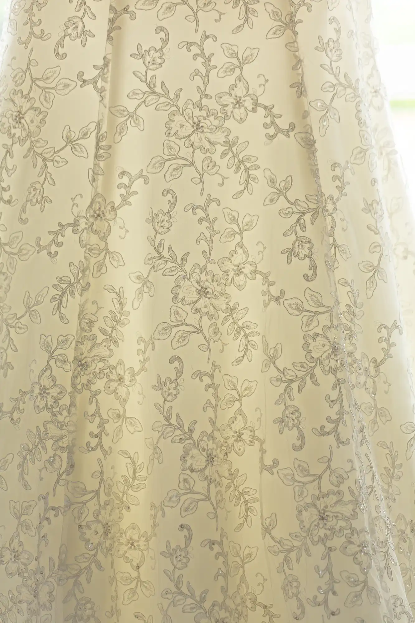 Sheer curtain with an embroidered floral pattern, backlit by natural light, creating a soft, translucent effect.