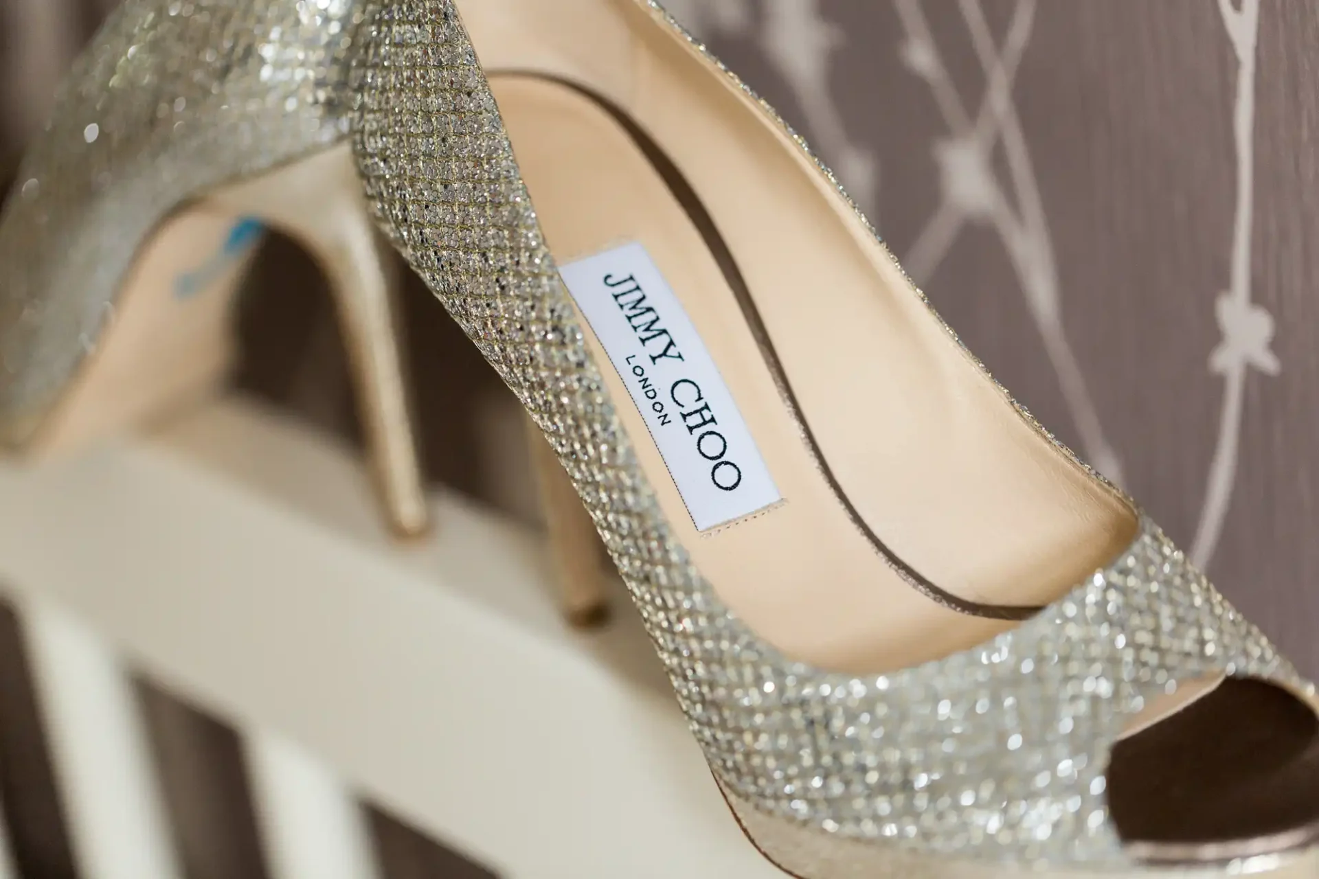 A close-up of a glittery silver jimmy choo high heel shoe displayed on a shelf.