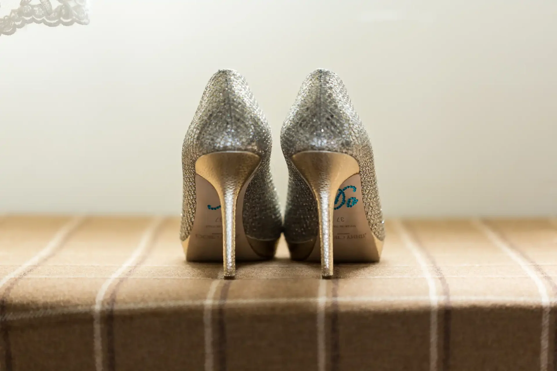 A pair of sparkly, silver high-heeled shoes placed back-to-back on a textured surface, with a soft, blurred background.