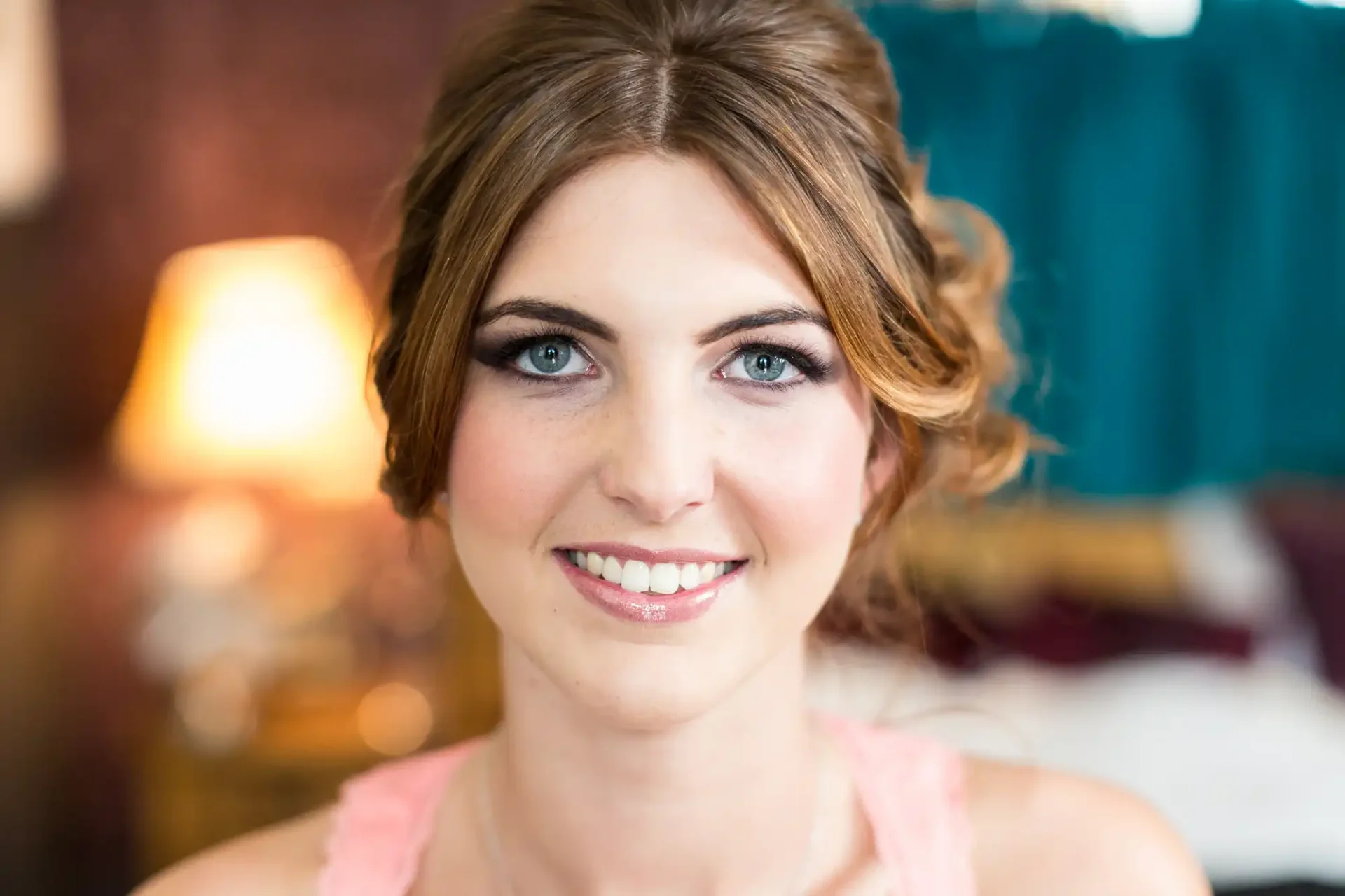 Close-up portrait of a smiling woman with blue eyes and styled brown hair, in a warmly lit room.