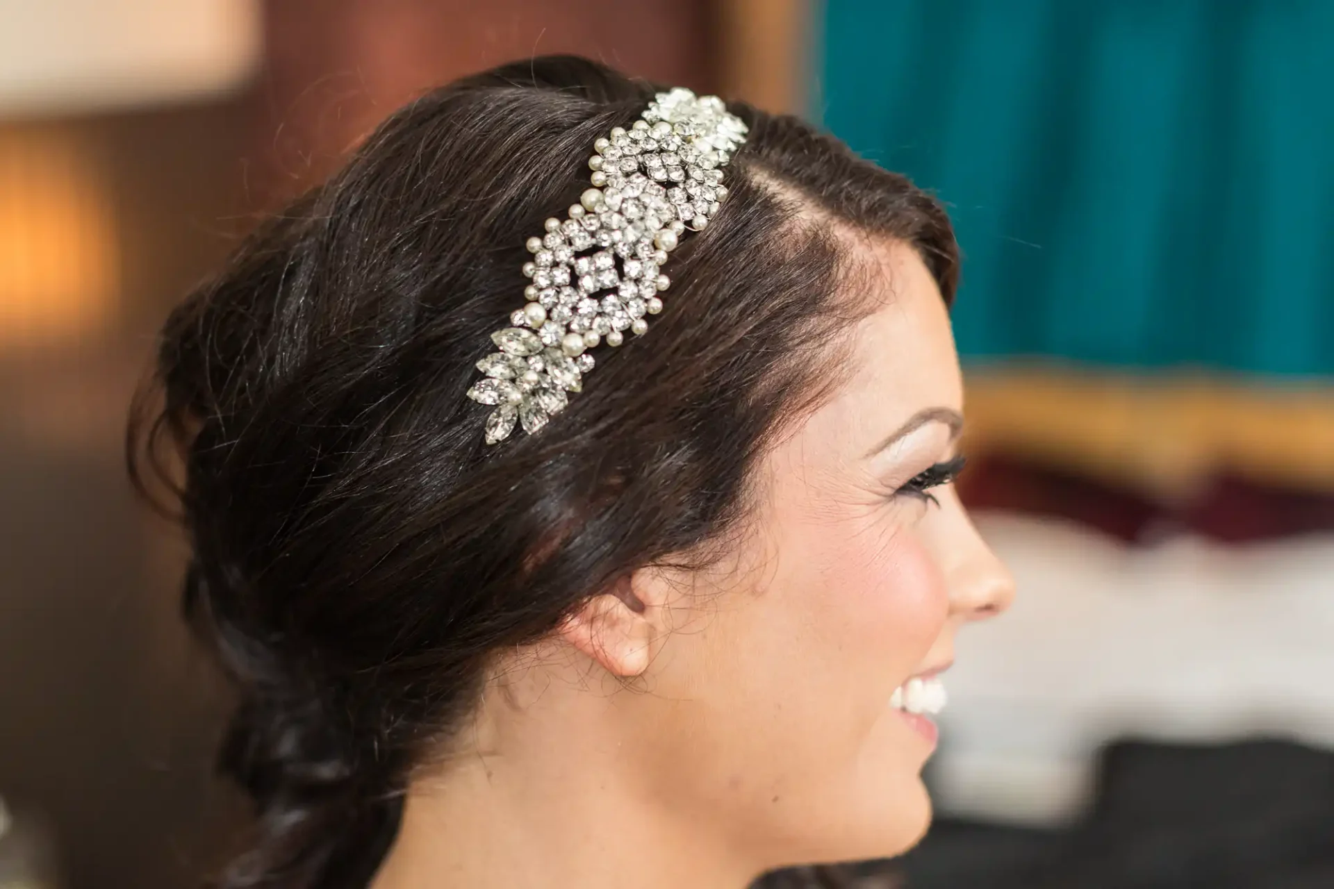 Side profile of a smiling woman with an elaborate rhinestone hair accessory in an elegant updo.