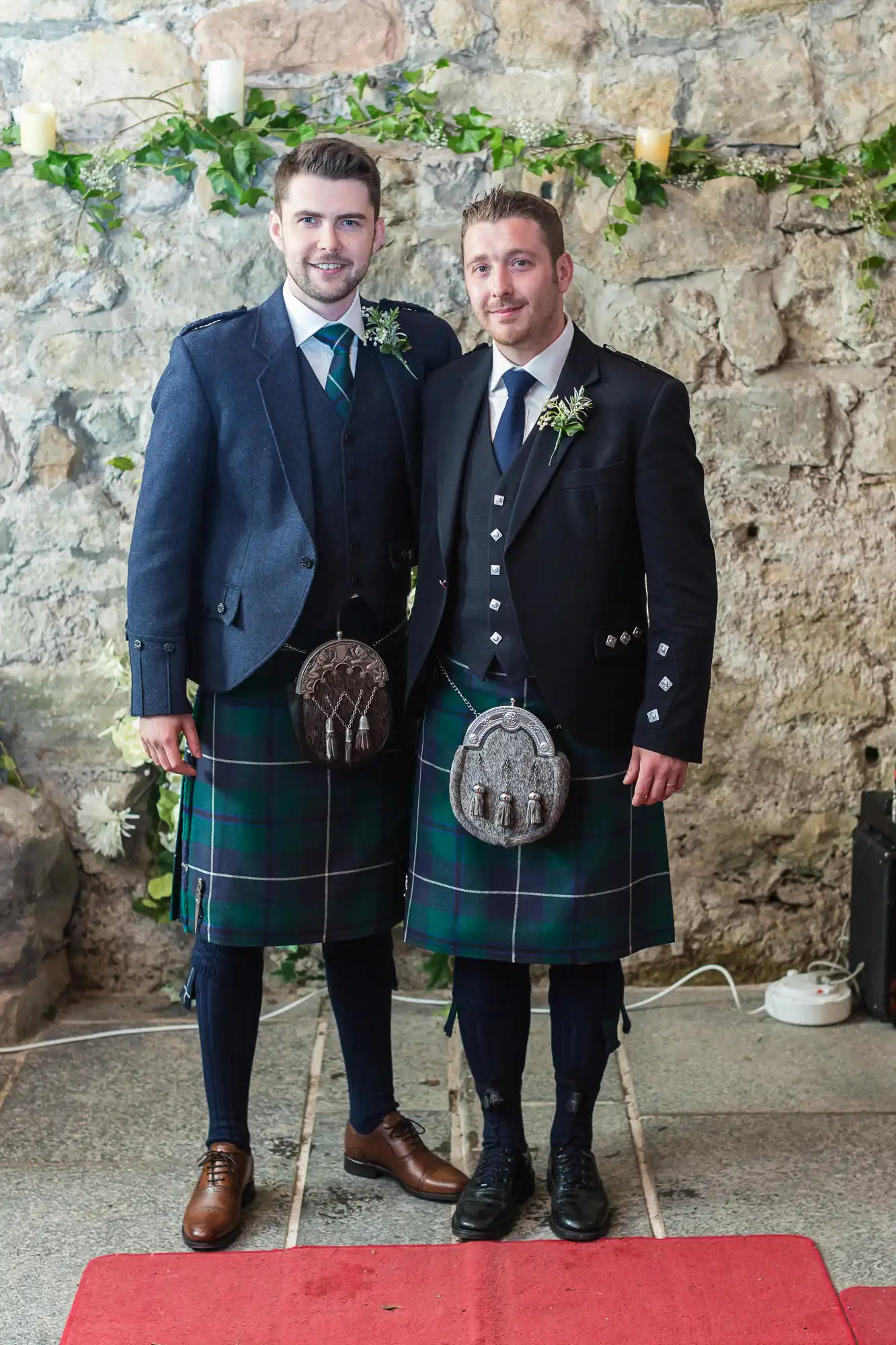 Two men in traditional scottish kilts and jackets standing together at an event, smiling for the camera.