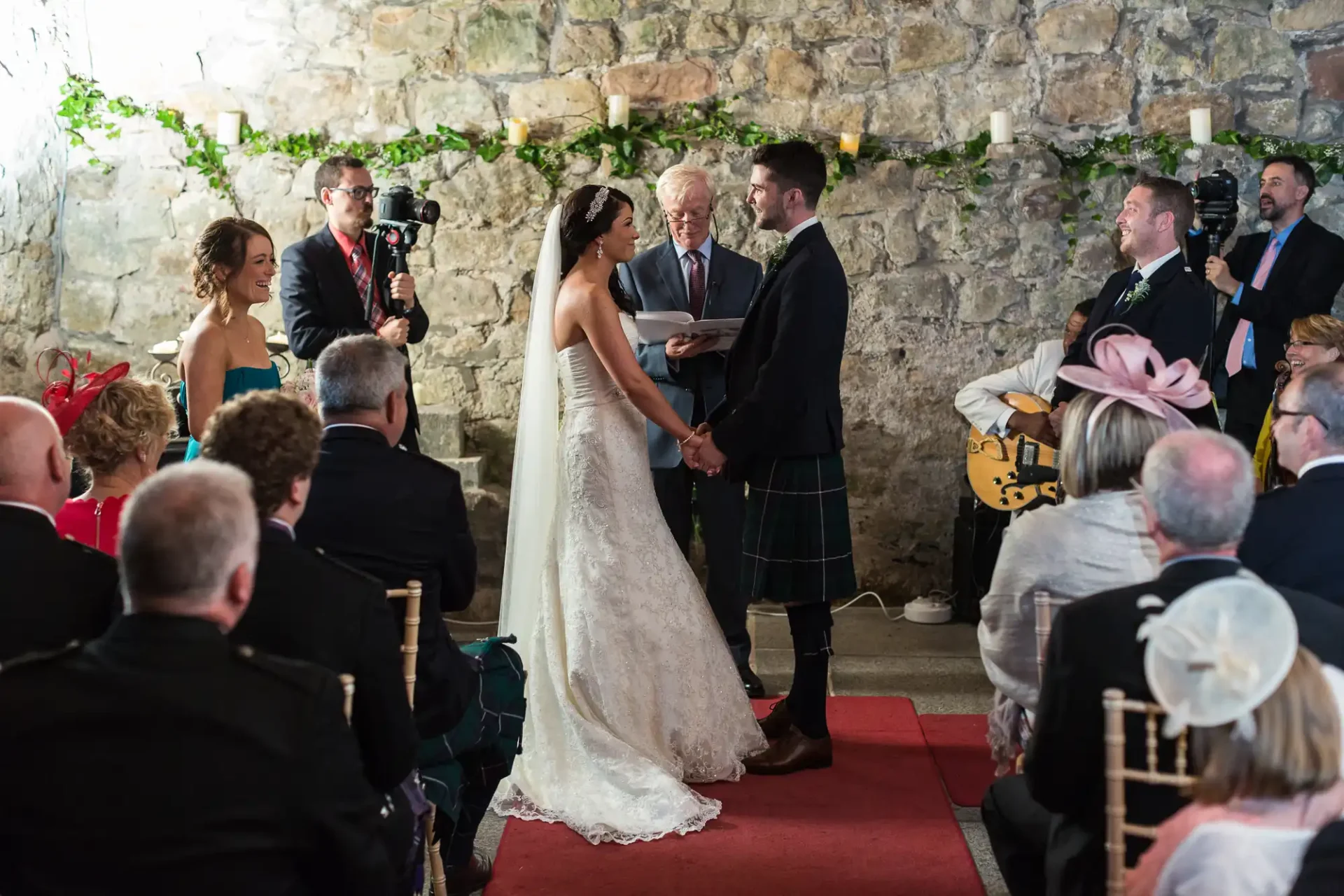 A wedding ceremony inside a rustic stone venue, featuring a bride and groom exchanging vows, with guests and a photographer capturing the moment.