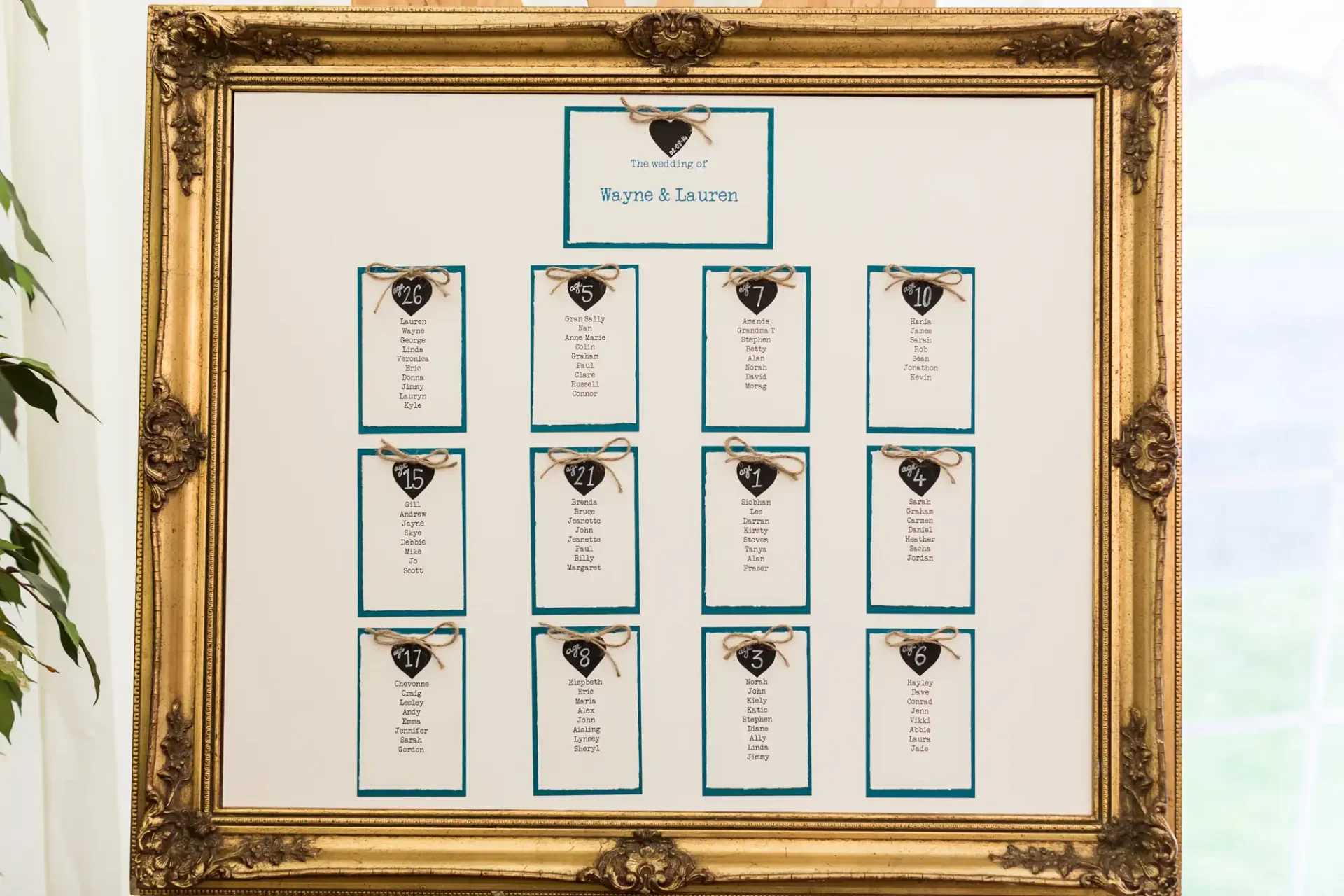 Ornate gold-framed seating chart for a wedding, featuring elegantly printed tables and guest names on a pale background, prominently displayed at an event.