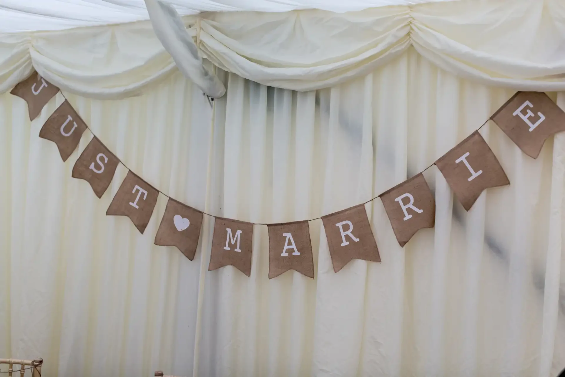 A burlap banner with the words "just married" hanging inside a white tent with draped linens.