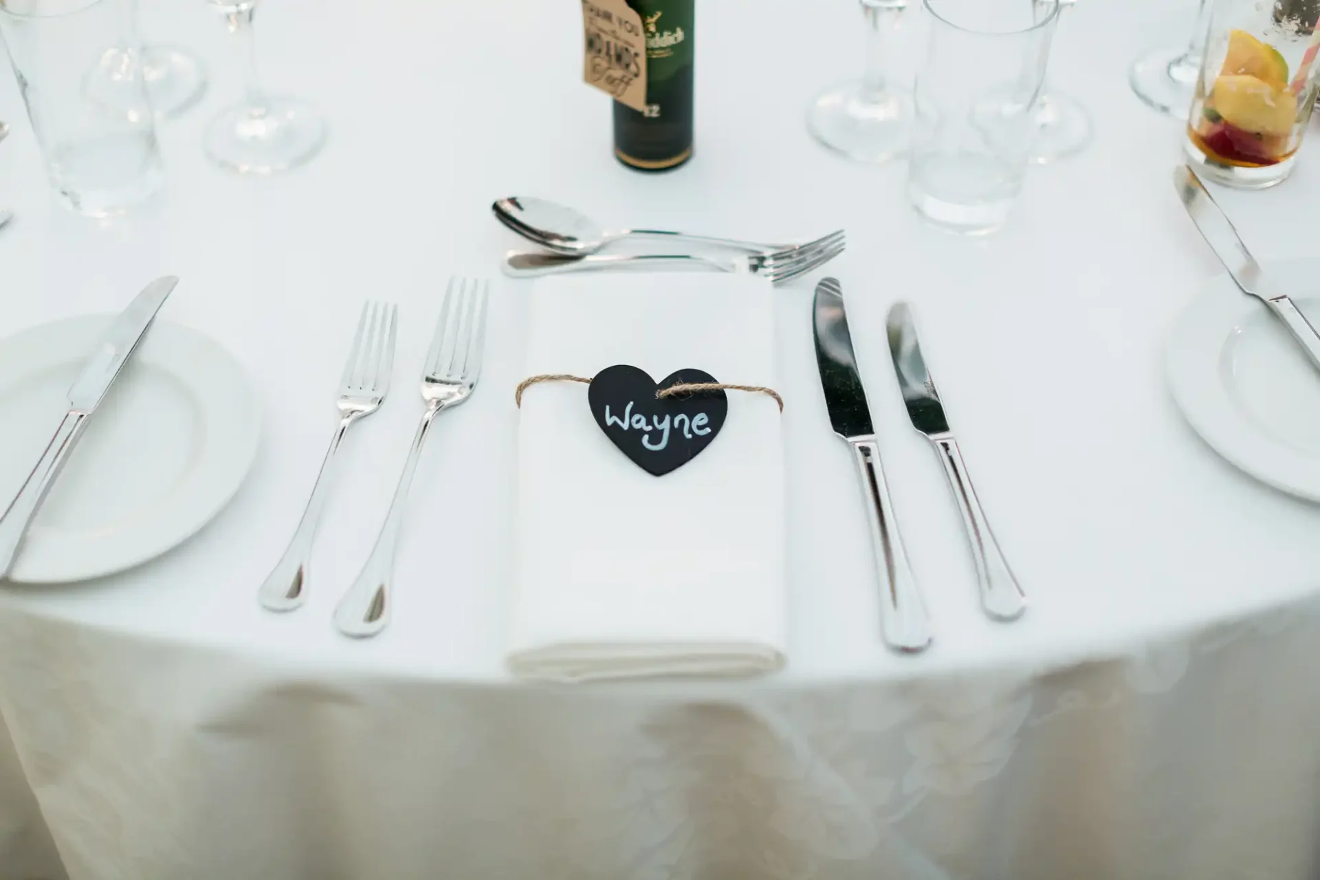 Elegant table setting with plates, glasses, cutlery, and a napkin tagged with a heart-shaped name card reading "wayne.