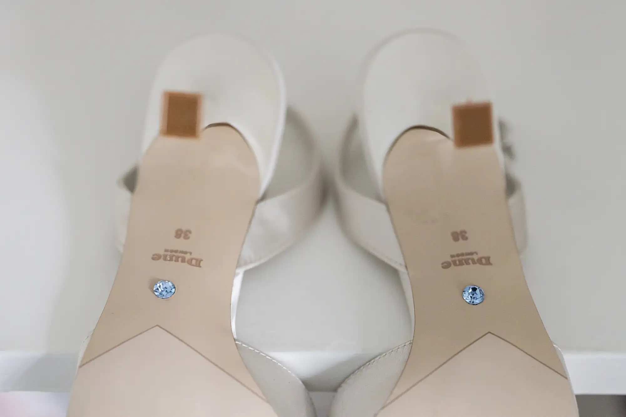 A pair of new white sandals with brown straps and blue crystal embellishments on the insoles, placed on a white surface.