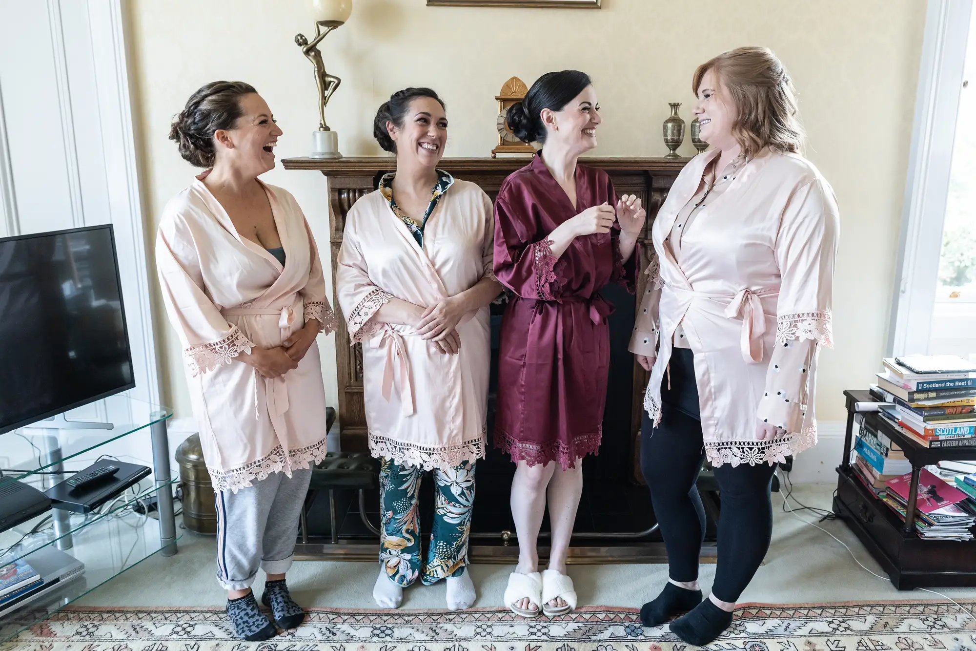 Four women in robes laughing together in a living room setting.