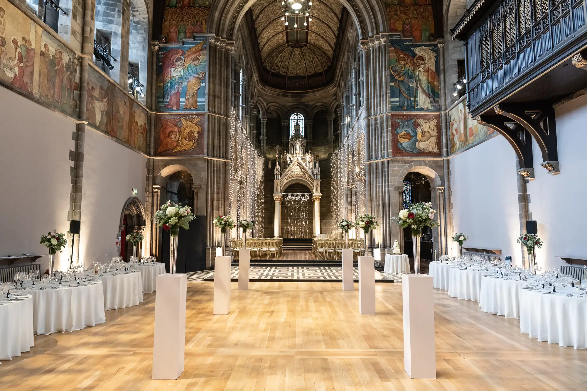 Elegant dining setup in a historic church with frescoed walls, ornate stained glass, and a grand altar, featuring white linen tables and floral arrangements.