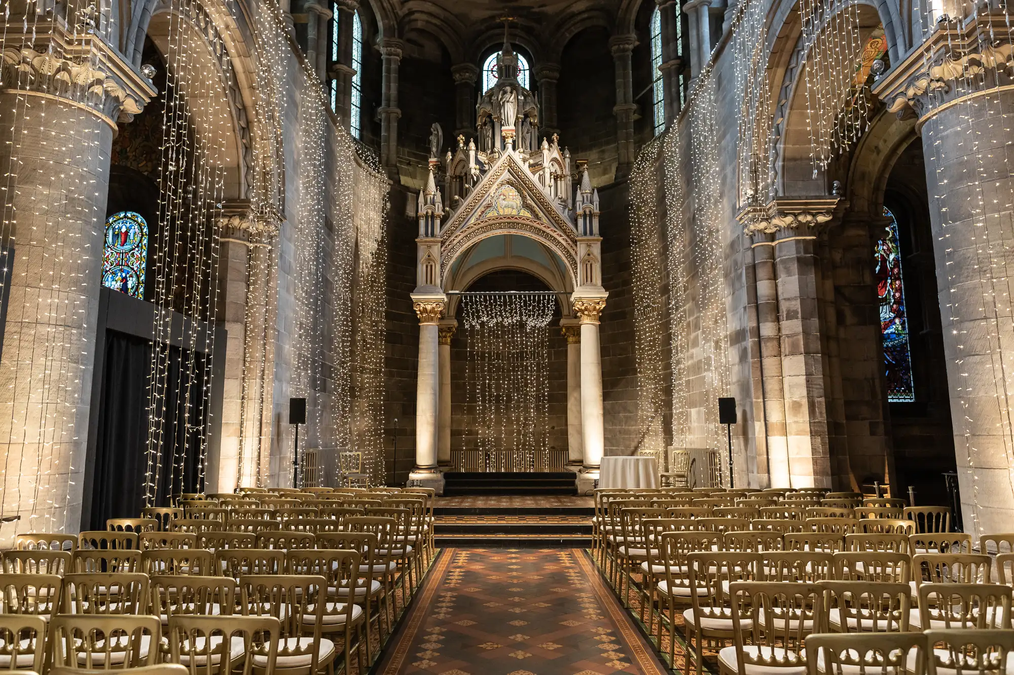 Interior of a gothic cathedral showing an arched ceiling, stained glass windows, and rows of chairs facing an ornate altar.
