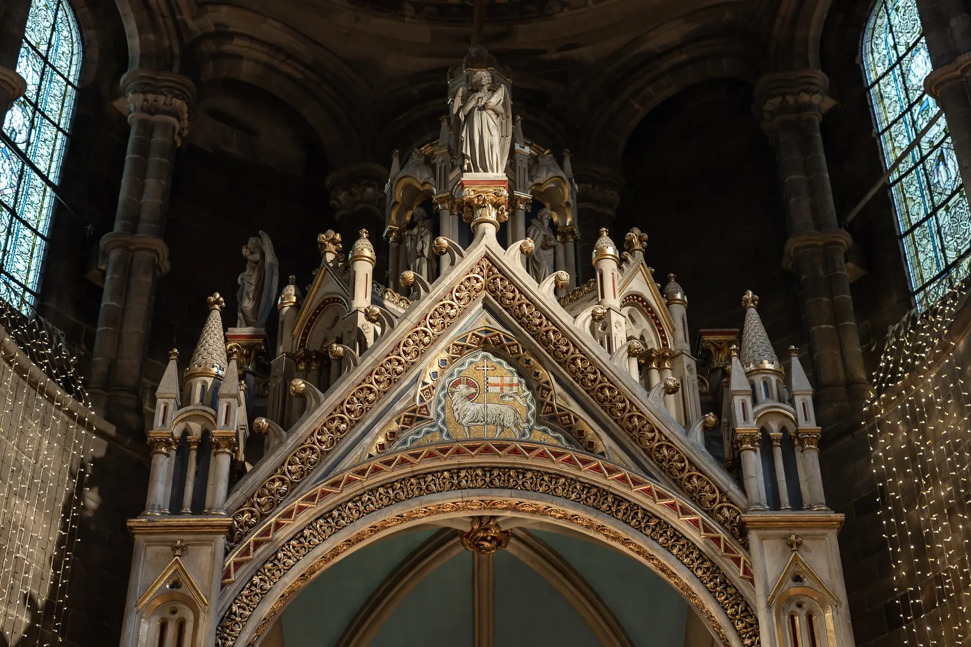 Ornate gothic arch inside a cathedral featuring sculptures, intricate patterns, and a lamb relief in the center.