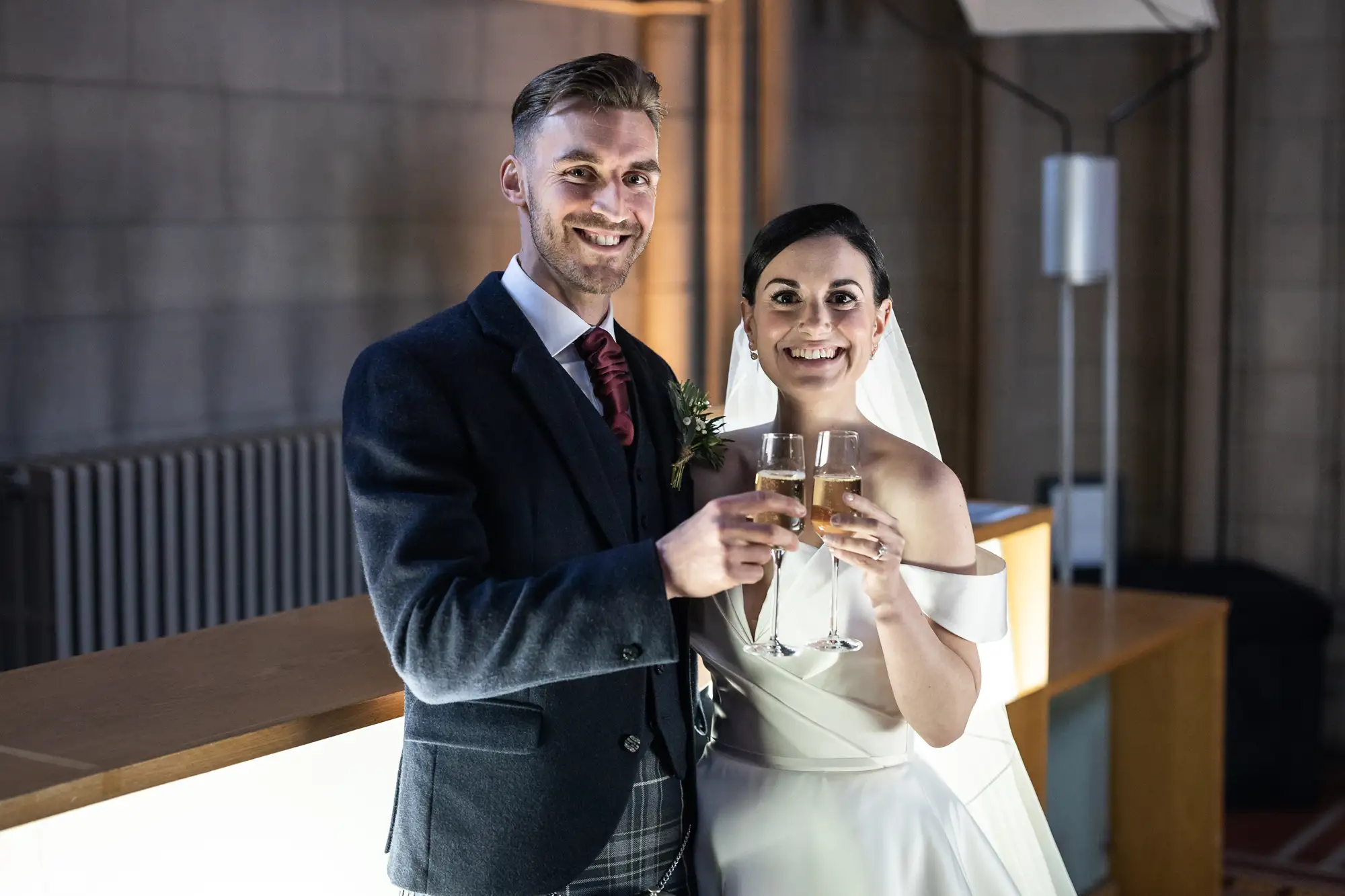 A bride and groom smiling and toasting with champagne glasses at their wedding reception.