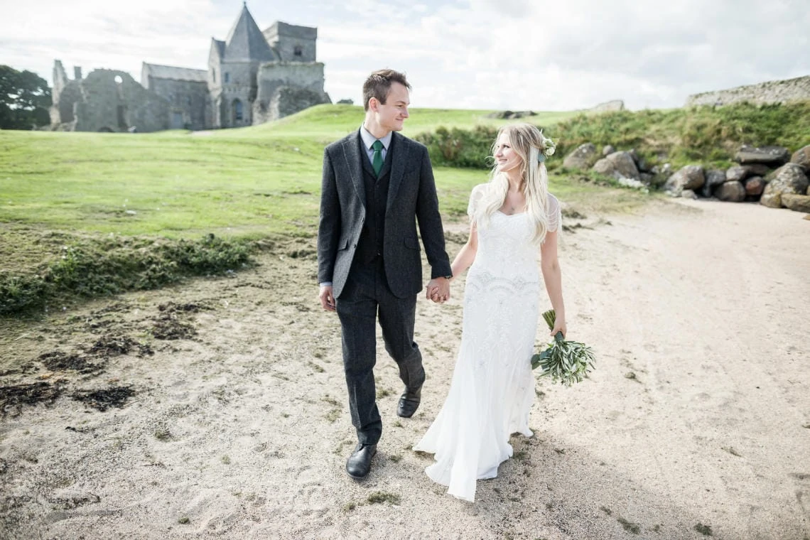 Newly-weds walking on the beach at Inchcolm Island with Inchcolm Abbey in the background